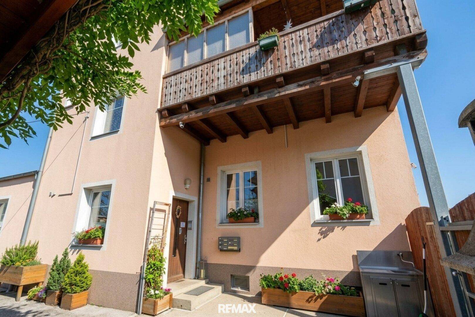 Rückansicht eines Wohnhauses mit traditionellem Holzbalkon und Blumenkästen, umgeben von viel Grün.