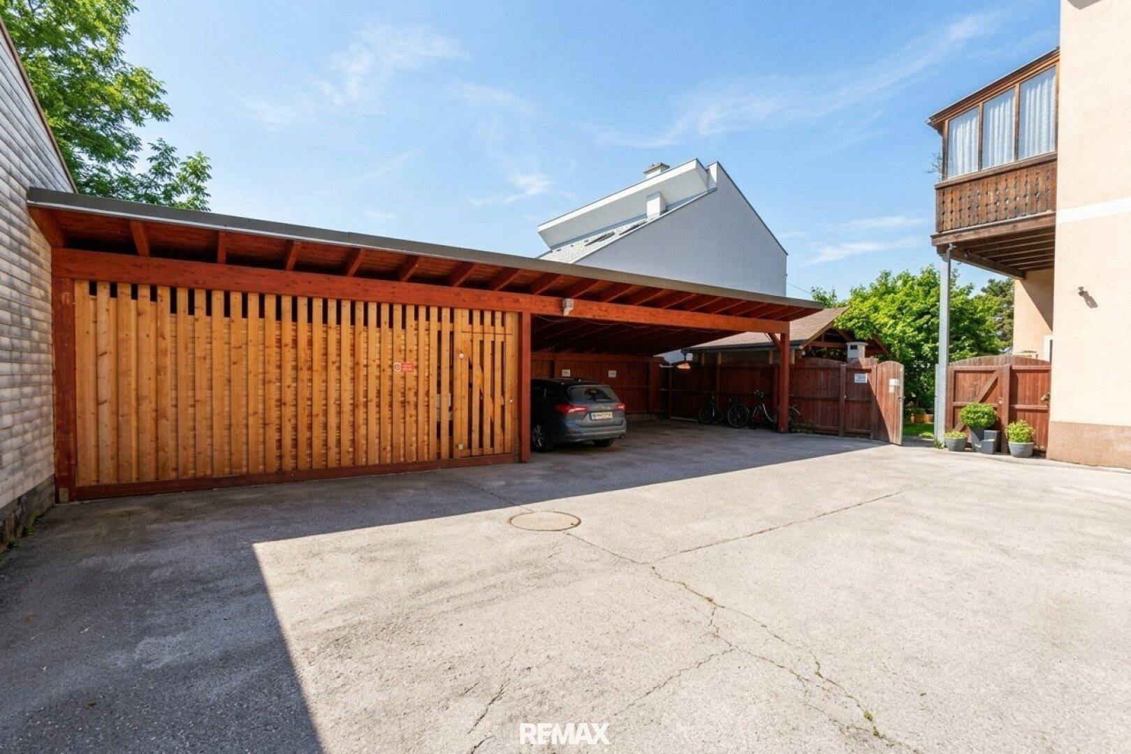 Geräumiger Carport aus Holz für mehrere Fahrzeuge, angrenzend an einen gepflasterten Bereich.