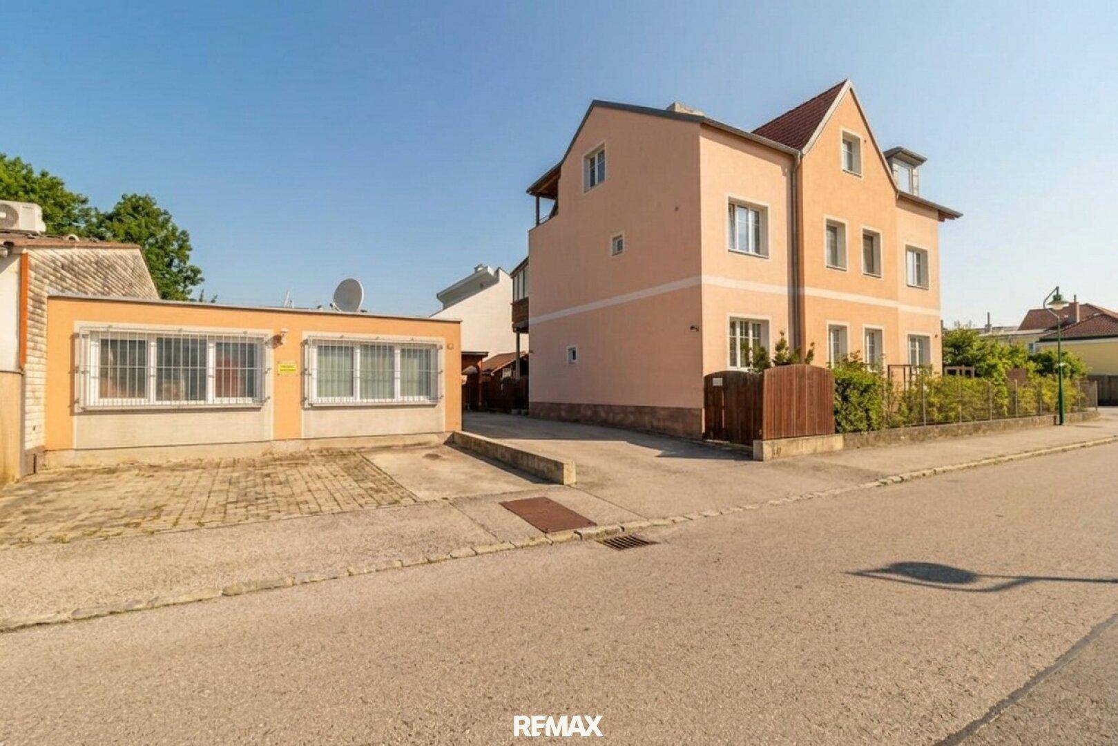 Ansicht des Wohnhauses von der Straße mit Nebengebäude und gepflasterter Zufahrt unter blauem Himmel.