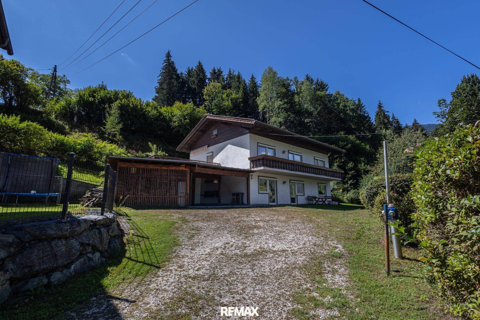 Ansicht des Hauses von der Einfahrt aus, umgeben von viel Grün und Bäumen unter blauem Himmel.