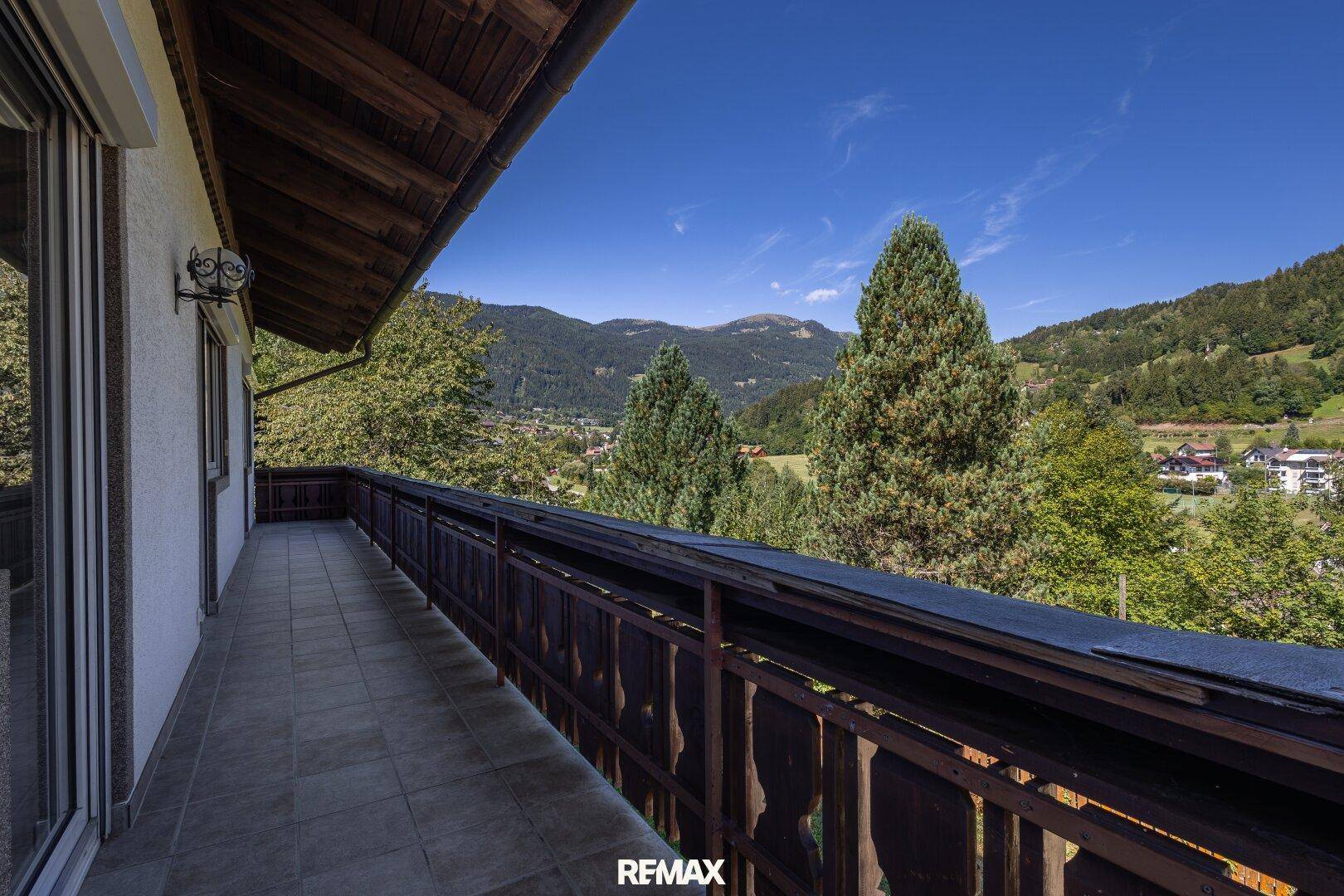 Langer Balkon mit Holzgeländer und Fliesenboden, bietet einen weiten Blick auf die umliegende Berglandschaft.