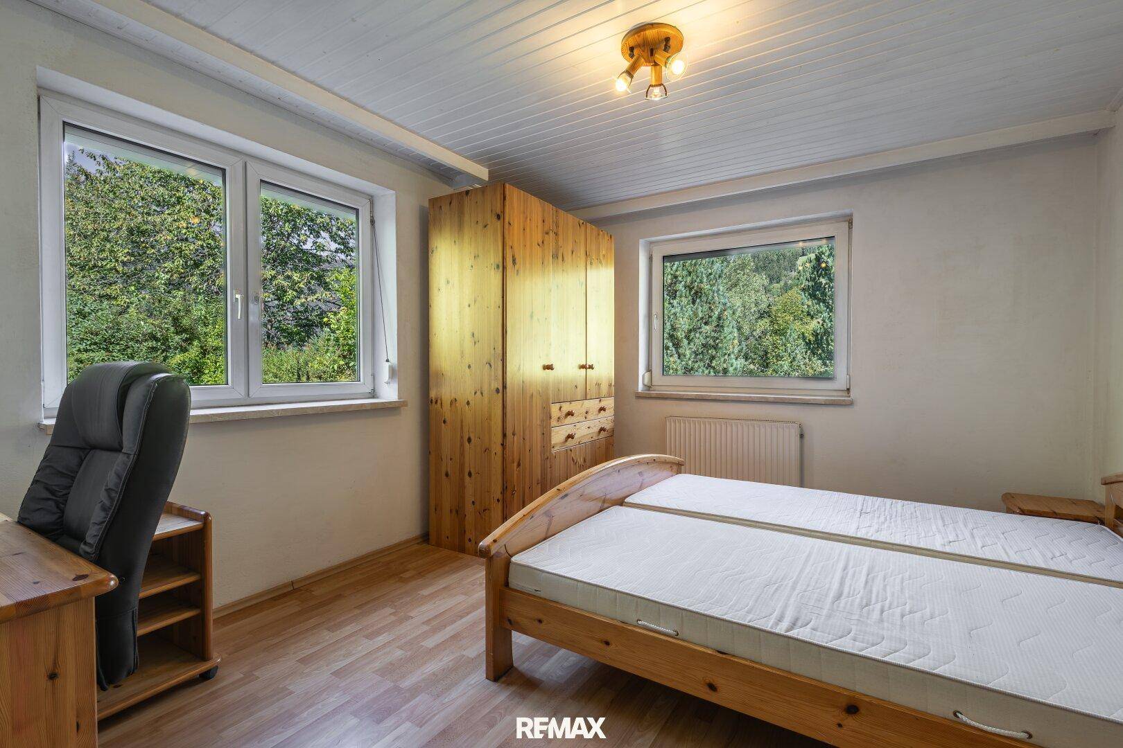 Schlafzimmer mit Holzmöbeln, Laminatboden und Blick ins Grüne durch die Fenster.