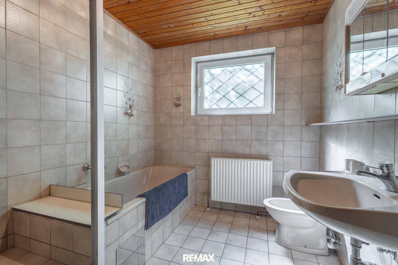 Gefliestes Badezimmer mit Badewanne, Waschbecken und Fenster, ausgestattet im traditionellen Stil.