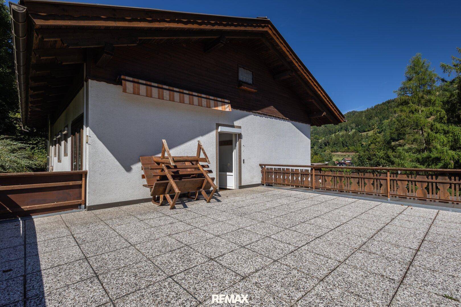 Große geflieste Terrasse mit Holzzaun und Blick auf die umliegende Berglandschaft.