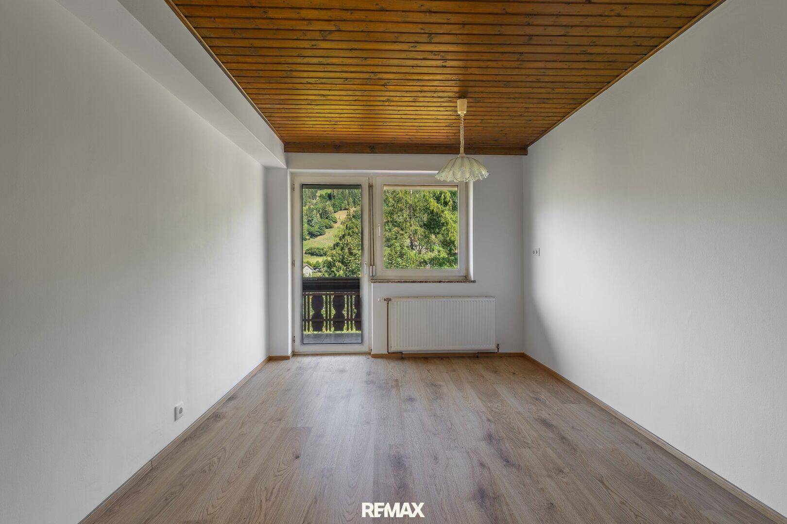 Schlafzimmer mit Laminatboden, Holzdecke und Zugang zu einem kleinen Balkon mit Bergblick.