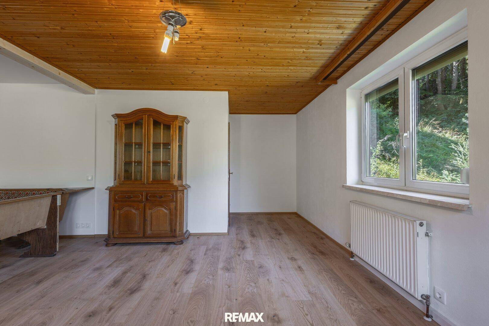 Teil eines Wohnbereichs mit Holzbalkendecke, Laminatboden und einem traditionellen Holzschrank.