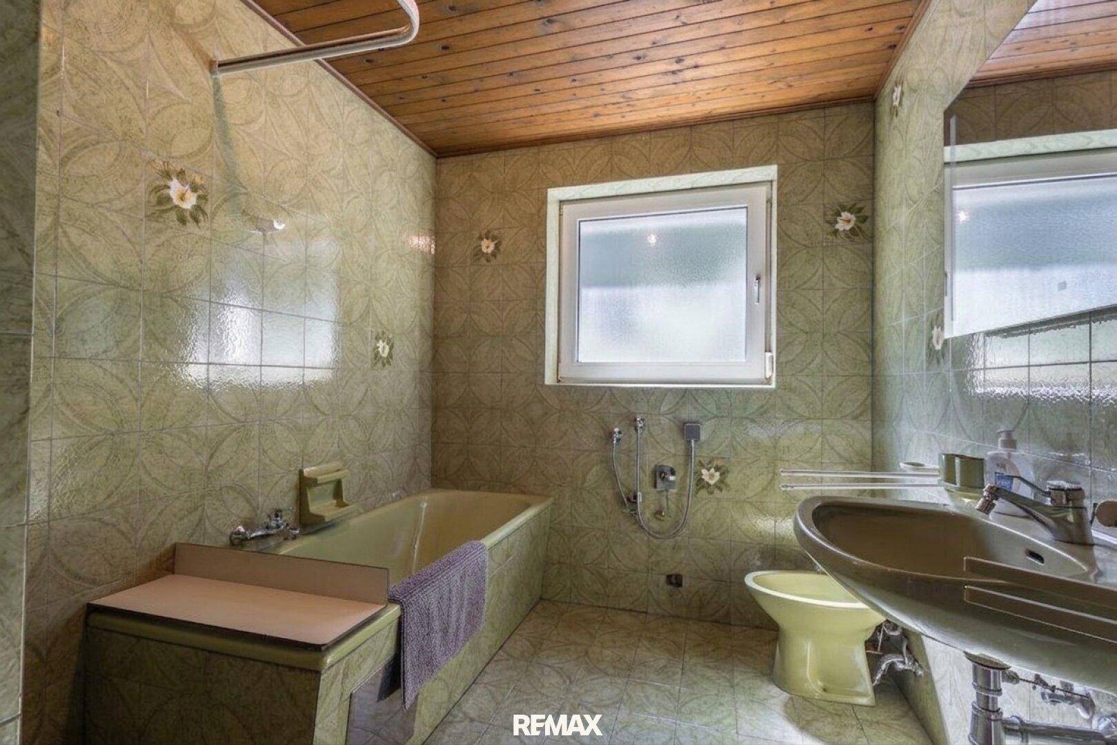 Badezimmer mit grünen Fliesen, Badewanne, Waschbecken und Fenster, im Stil der 80er Jahre.