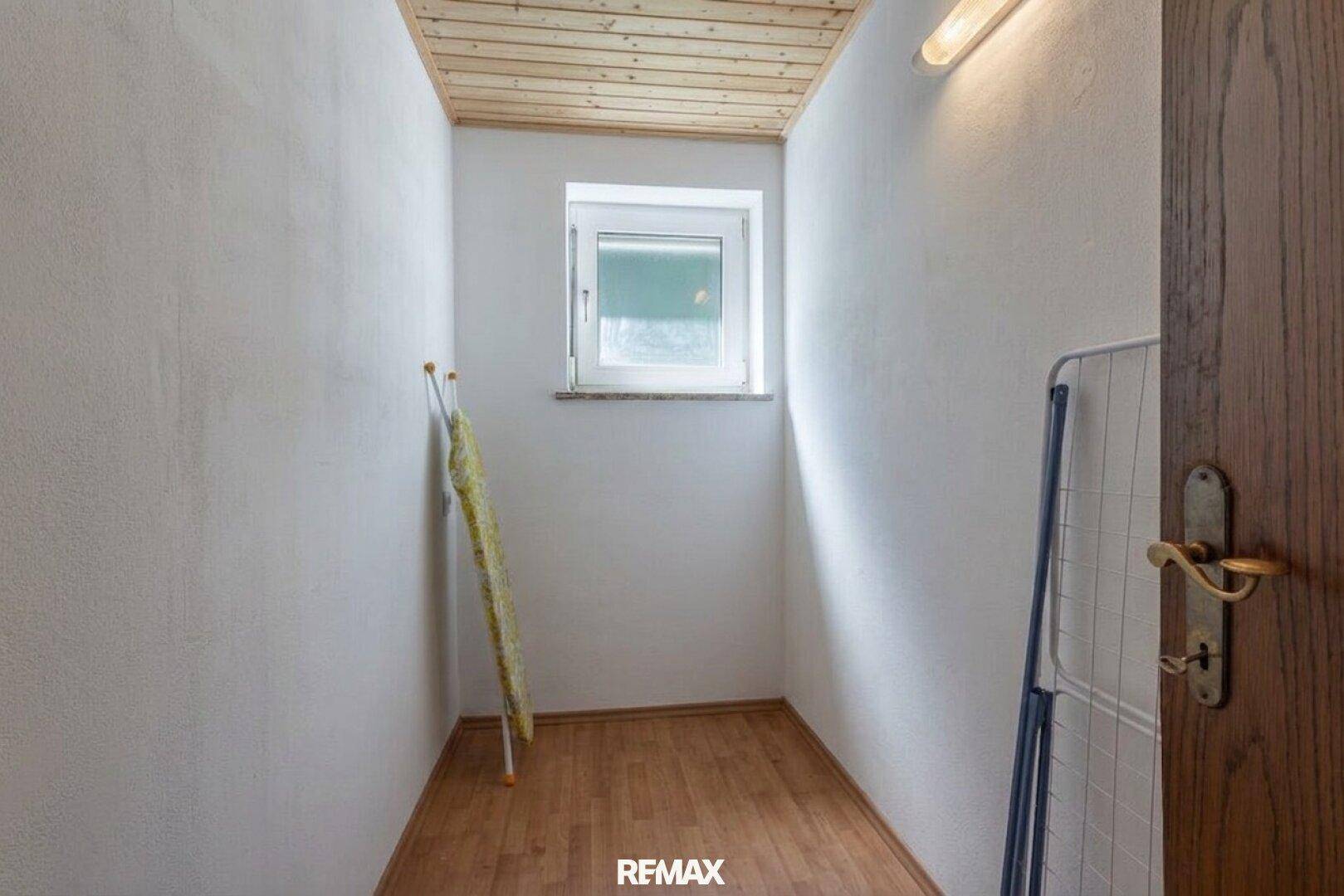 Kleiner Abstellraum mit Fenster, Holzboden und einem Wäscheständer, ideal als Hauswirtschaftsraum.