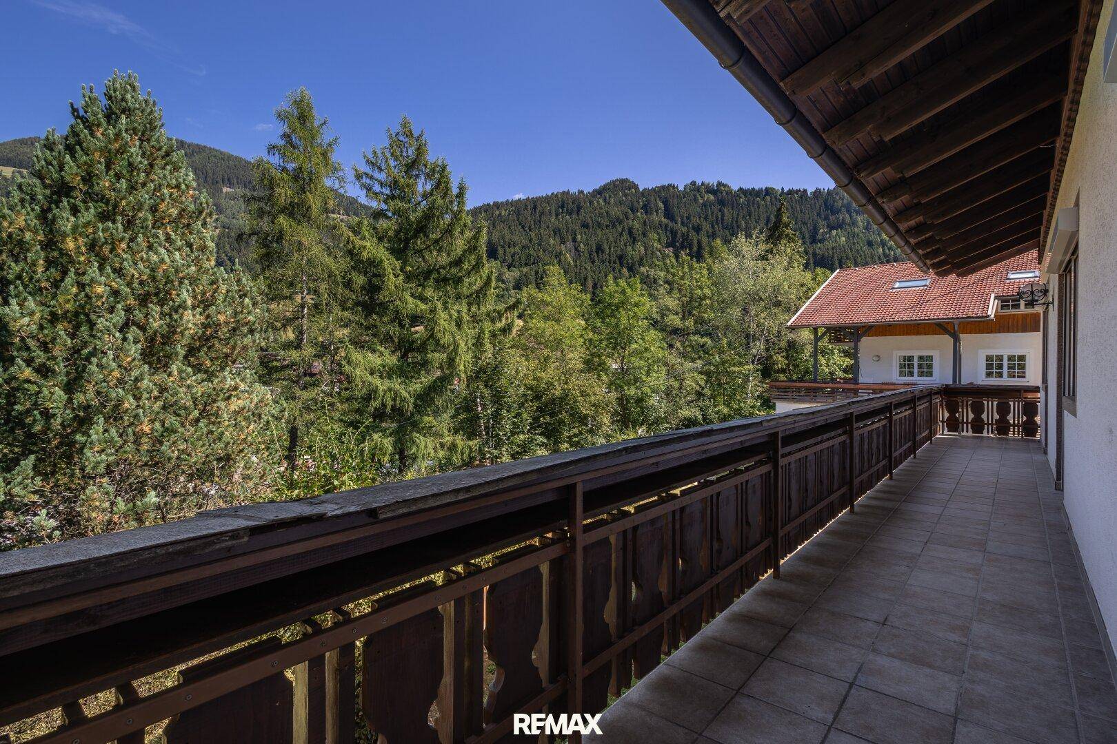 Langer Balkon mit Holzbalkongeländer, Fliesenboden und einem schönen Blick auf die umliegenden Berge.