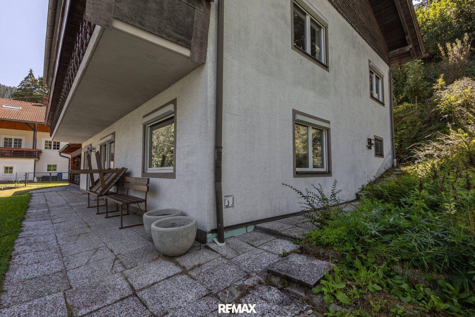 Seitenansicht des Hauses mit gepflastertem Weg, Stufen und üppiger, teils wilder Bepflanzung.