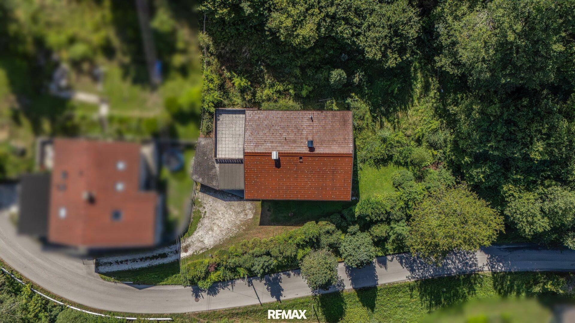 Luftaufnahme des Anwesens mit rotem Ziegeldach, umgeben von viel Grün und einer Straße.
