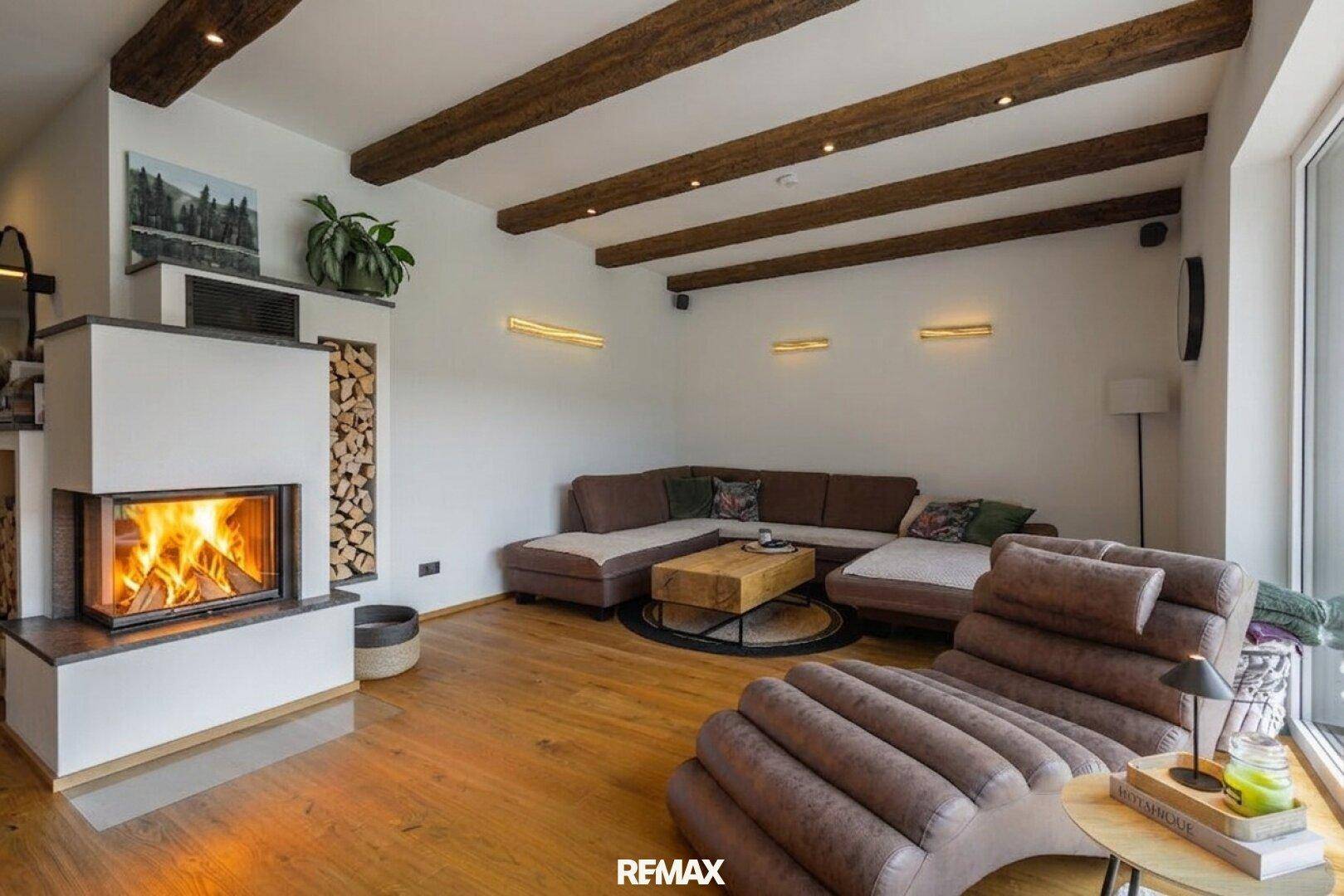 Gemütliches Wohnzimmer mit Kamin, Holzbalken an der Decke und bequemer Sitzecke.