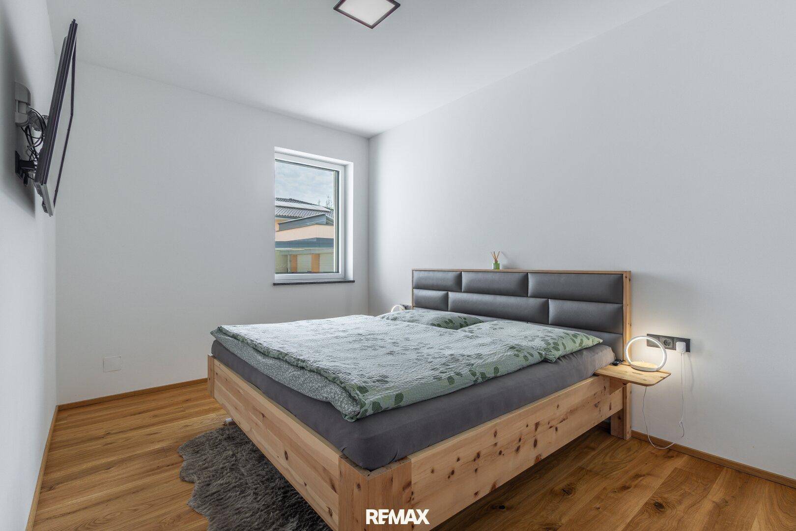 Schlafzimmer mit Holzbett, Holzboden und schlichten weißen Wänden.