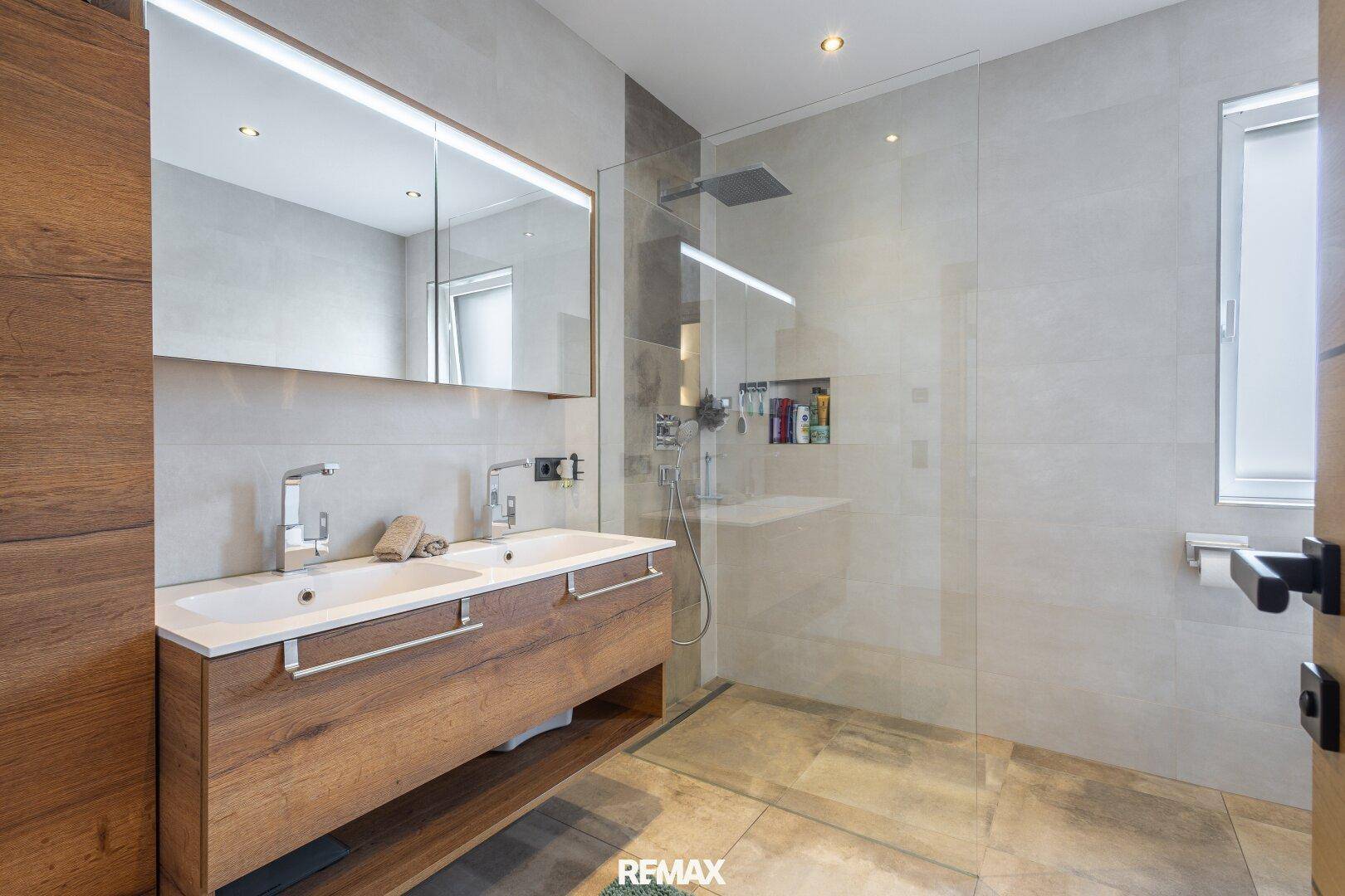 Modernes Badezimmer mit Doppelwaschbecken, großer begehbarer Dusche und hellen Fliesen.