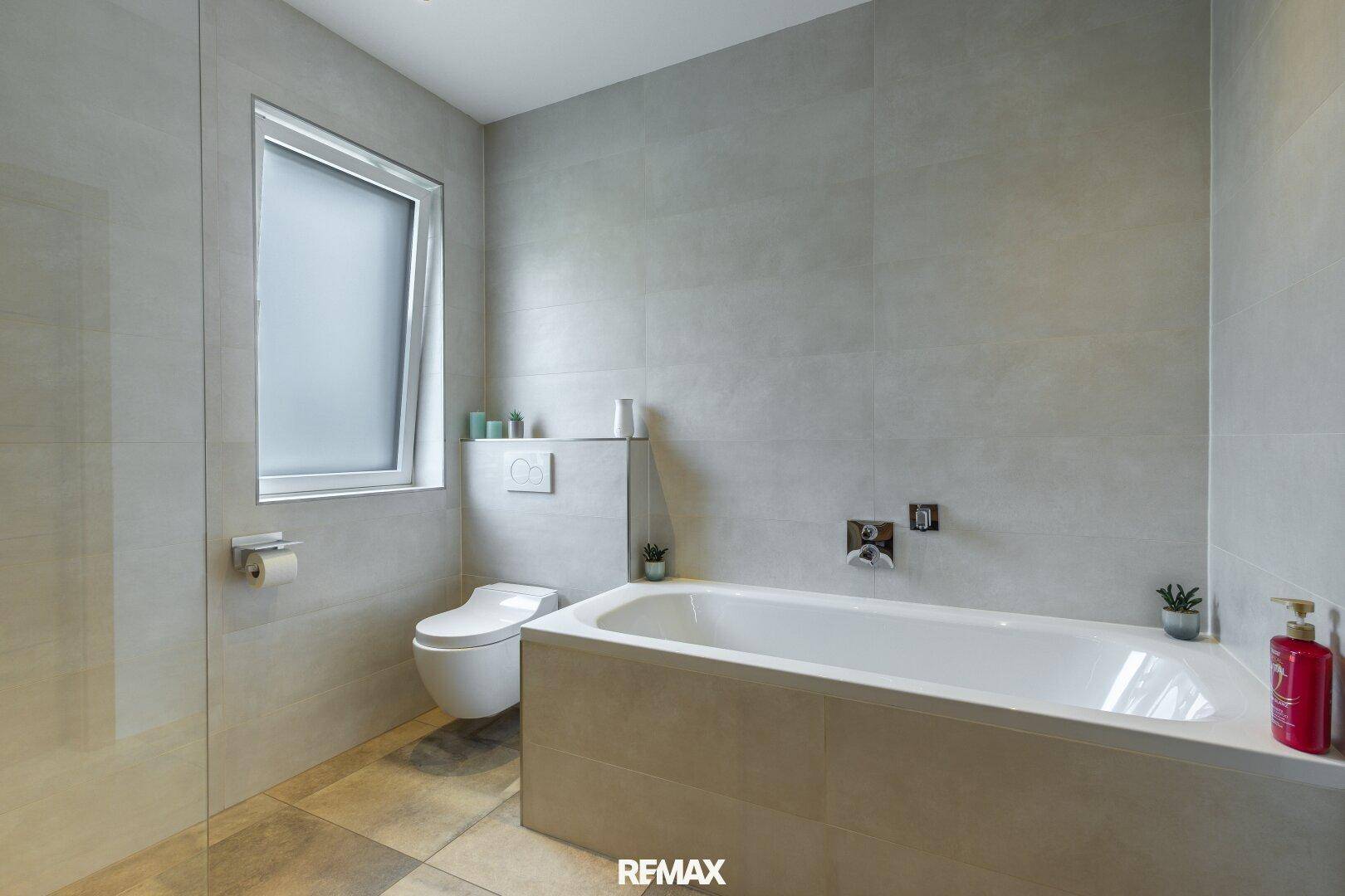 Modernes Badezimmer mit Badewanne, wandhängendem WC und hellen Fliesen.