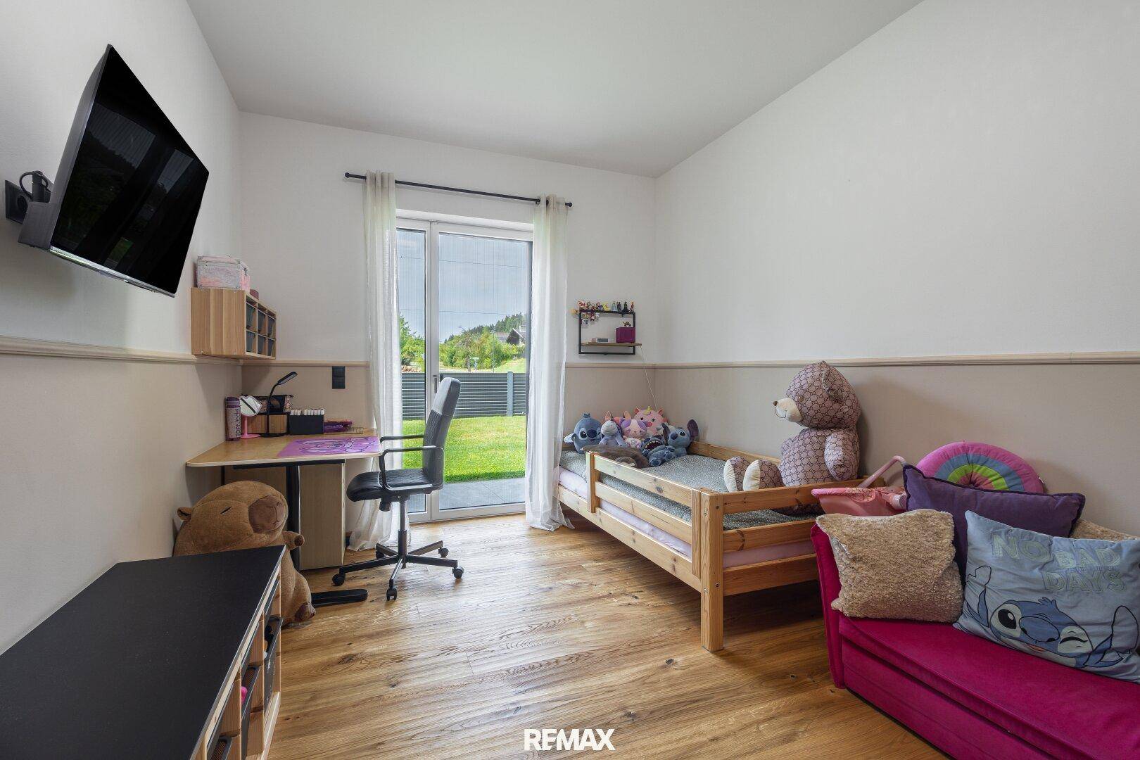 Helles Kinderzimmer mit Holzboden, Schreibtisch und direktem Zugang zum Garten.