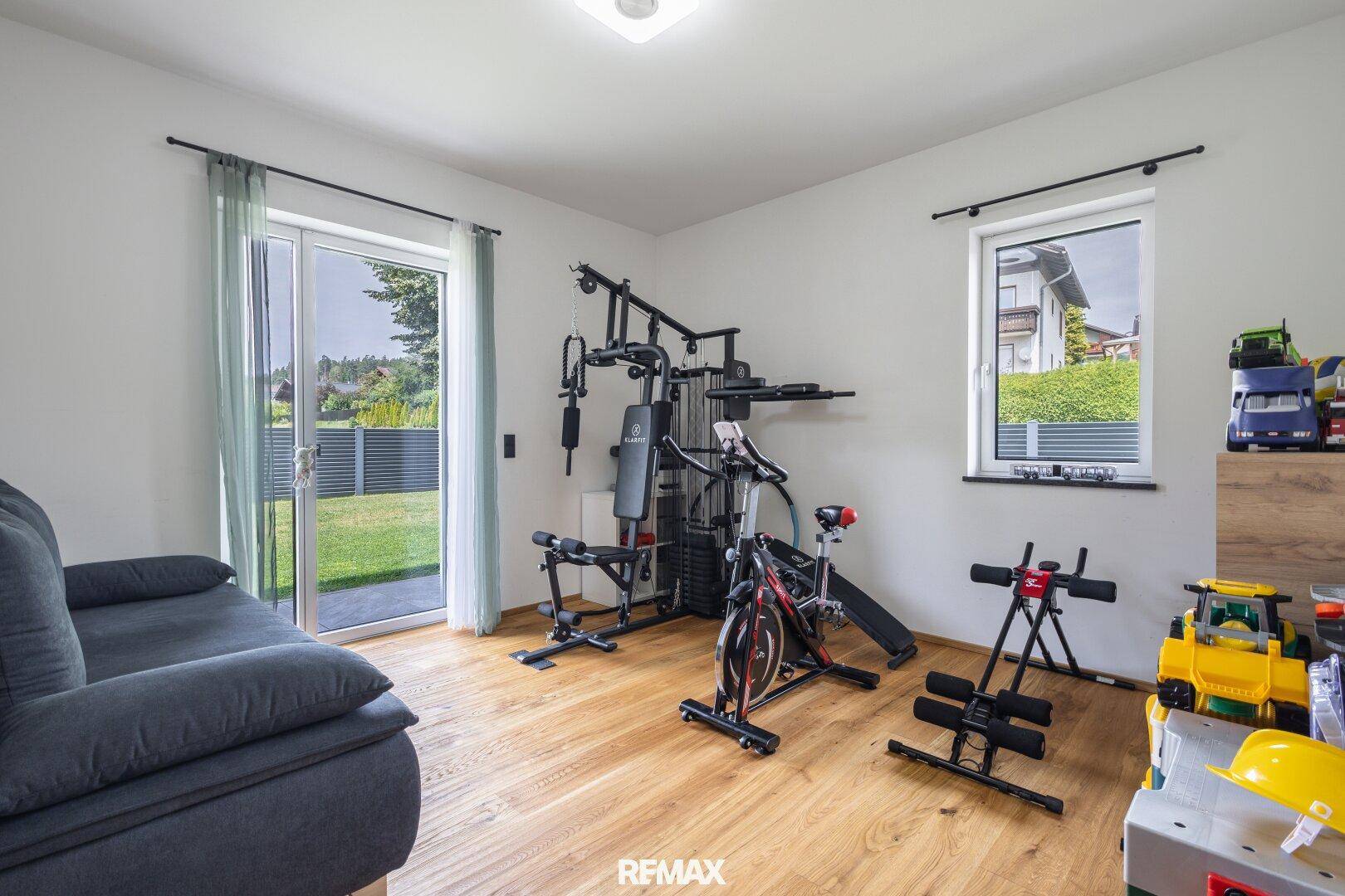 Raum mit Holzboden, Fitnessgeräten und Zugang zum Garten, auch als Spielzimmer nutzbar.