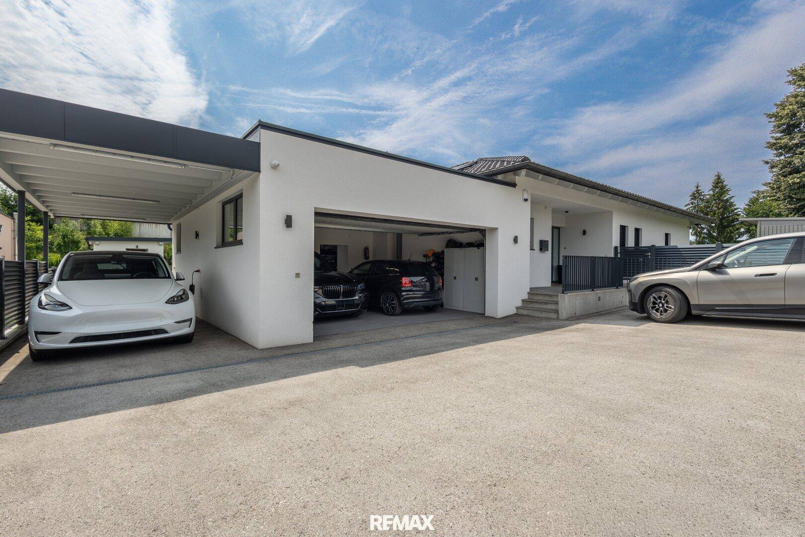 Moderne Hausfront mit Doppelgarage, Carport und großzügiger Auffahrt für mehrere Fahrzeuge.