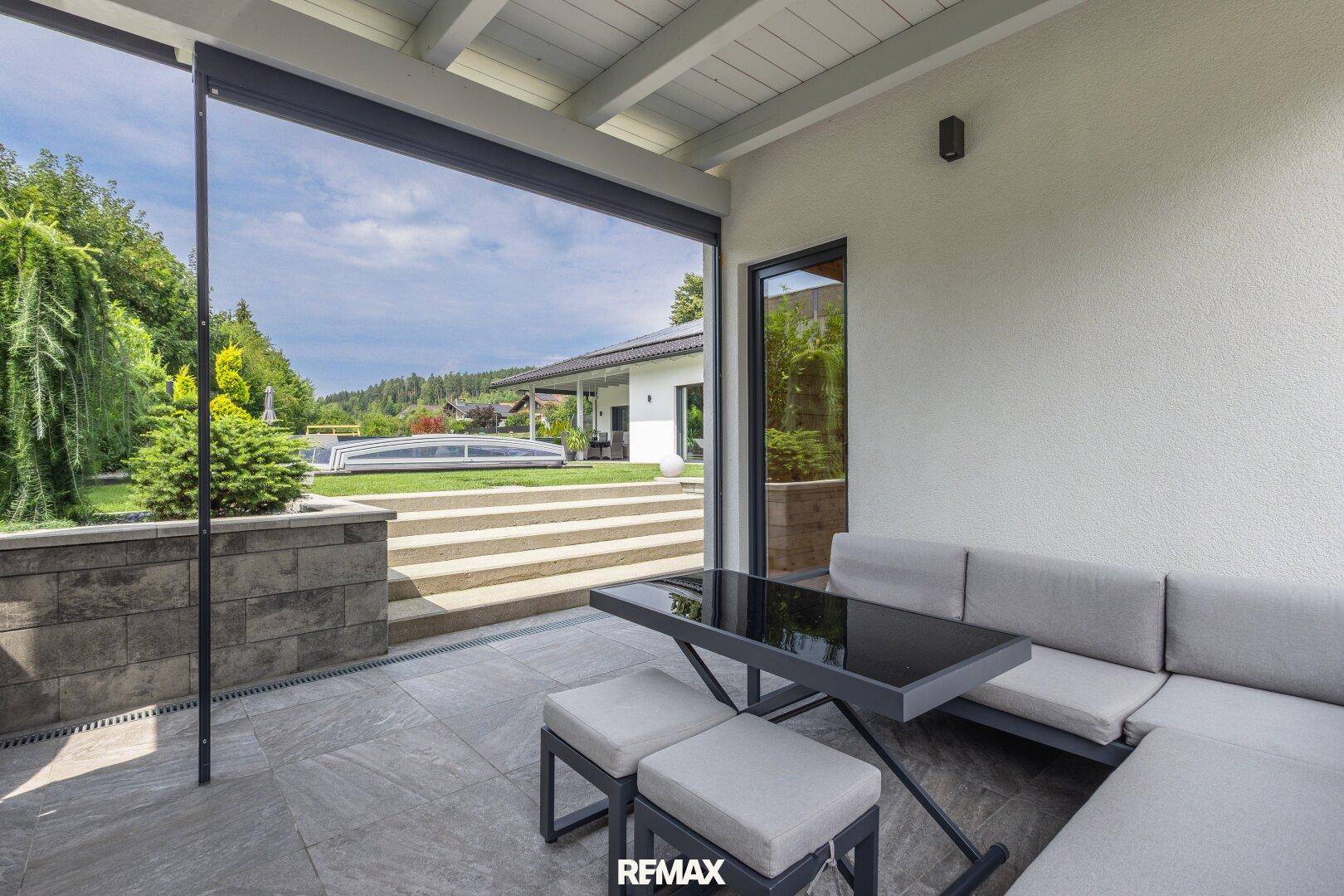 Gemütliche überdachte Terrasse mit Lounge-Möbeln und Blick auf den weitläufigen Garten und das Haupthaus.