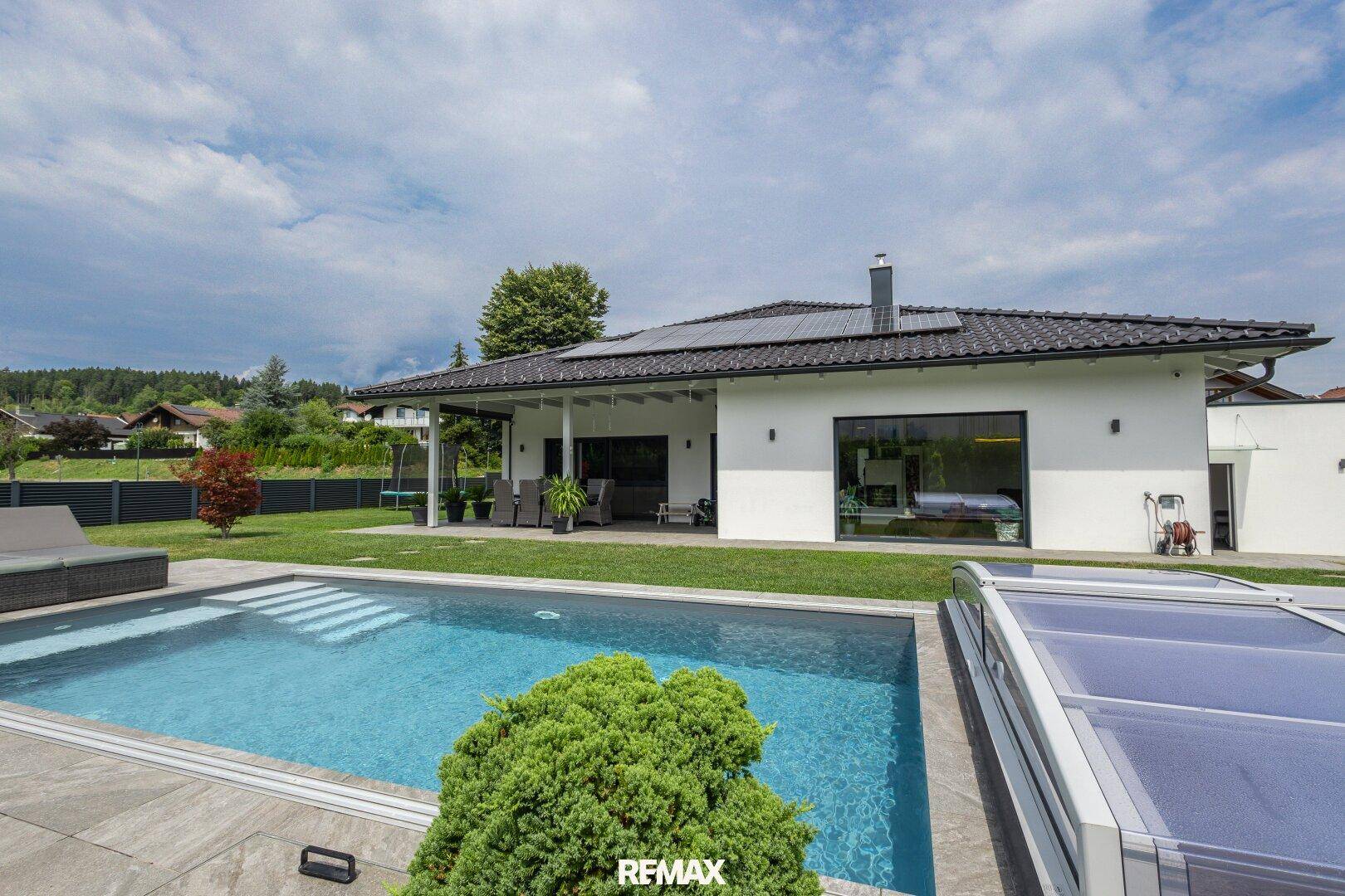 Weitläufiger Gartenbereich mit Swimmingpool und moderner Architektur des Hauses unter blauem Himmel.