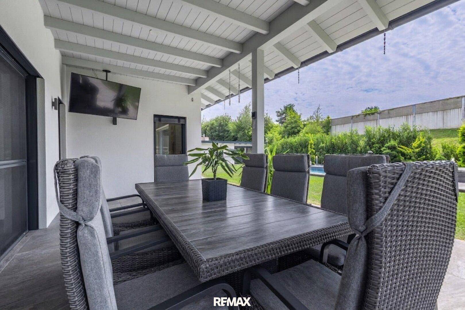 Geräumige überdachte Terrasse mit großem Esstisch und Blick in den Garten.