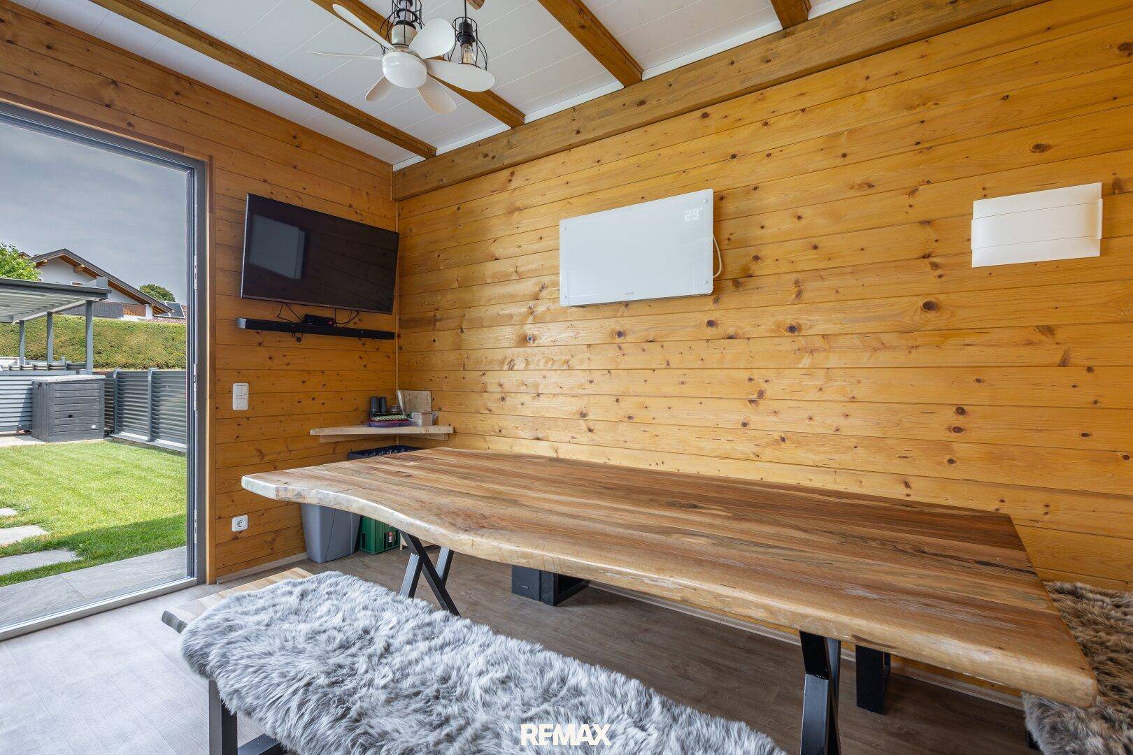 Heller Wintergarten mit Holzwänden, Fernseher und Schiebetür zum Garten, bietet viel Tageslicht.
