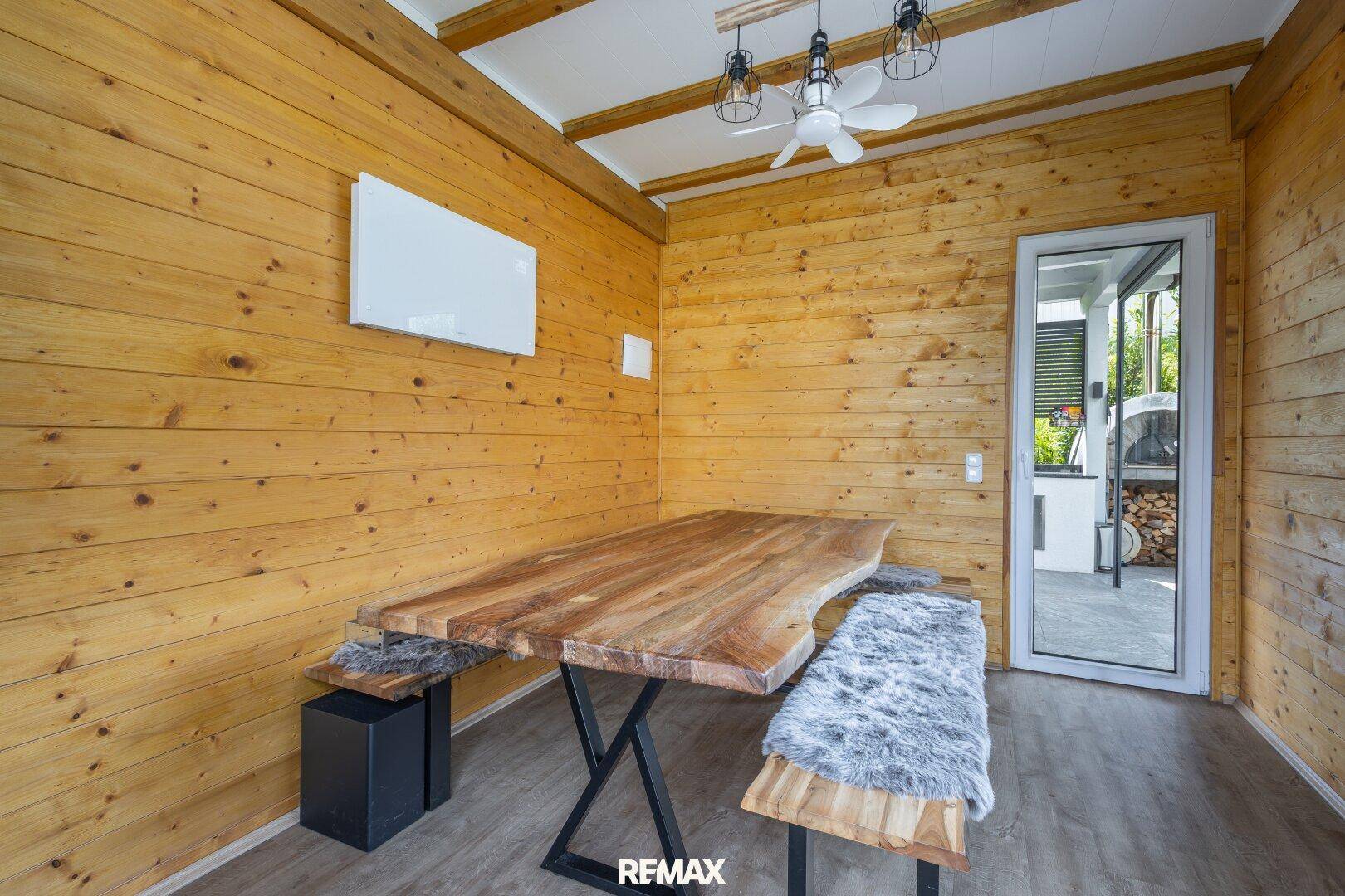 Rustikaler Wintergarten mit Holzwänden, großem Holztisch und Bänken, ideal für gesellige Runden.