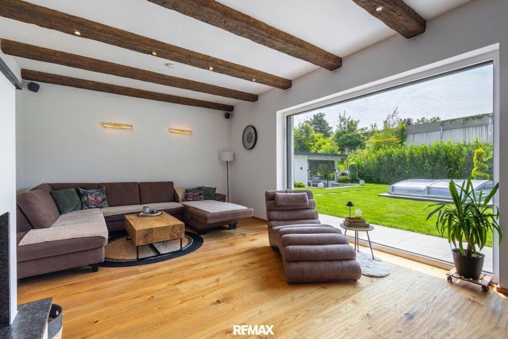 Helles Wohnzimmer mit großen Fenstern, Gartenblick und Holzbalken an der Decke.