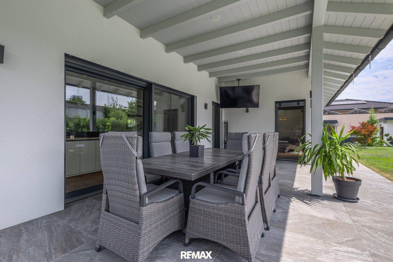 Helle überdachte Terrasse mit modernem Esstisch und Zugang zum Garten.