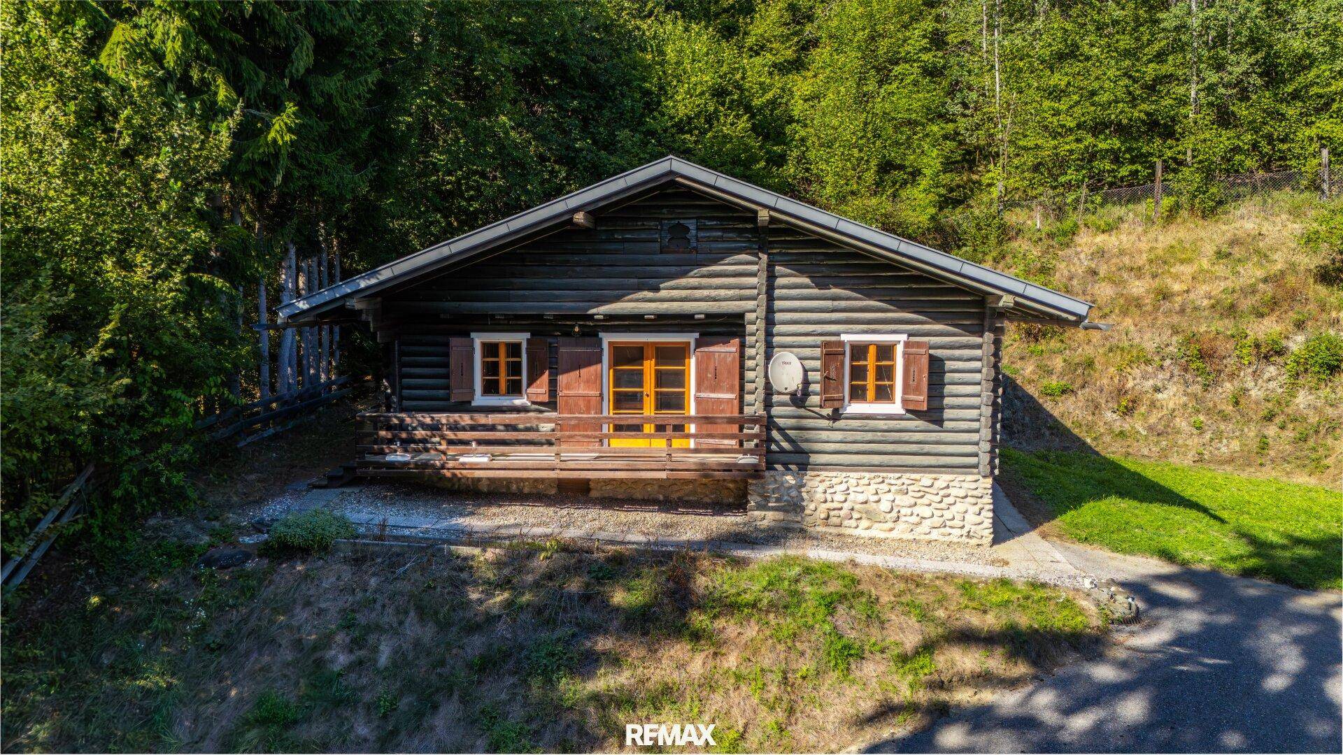 Charmantes Holzhaus mit traditionellen Fensterläden, umgeben von üppiger Vegetation und Wald.