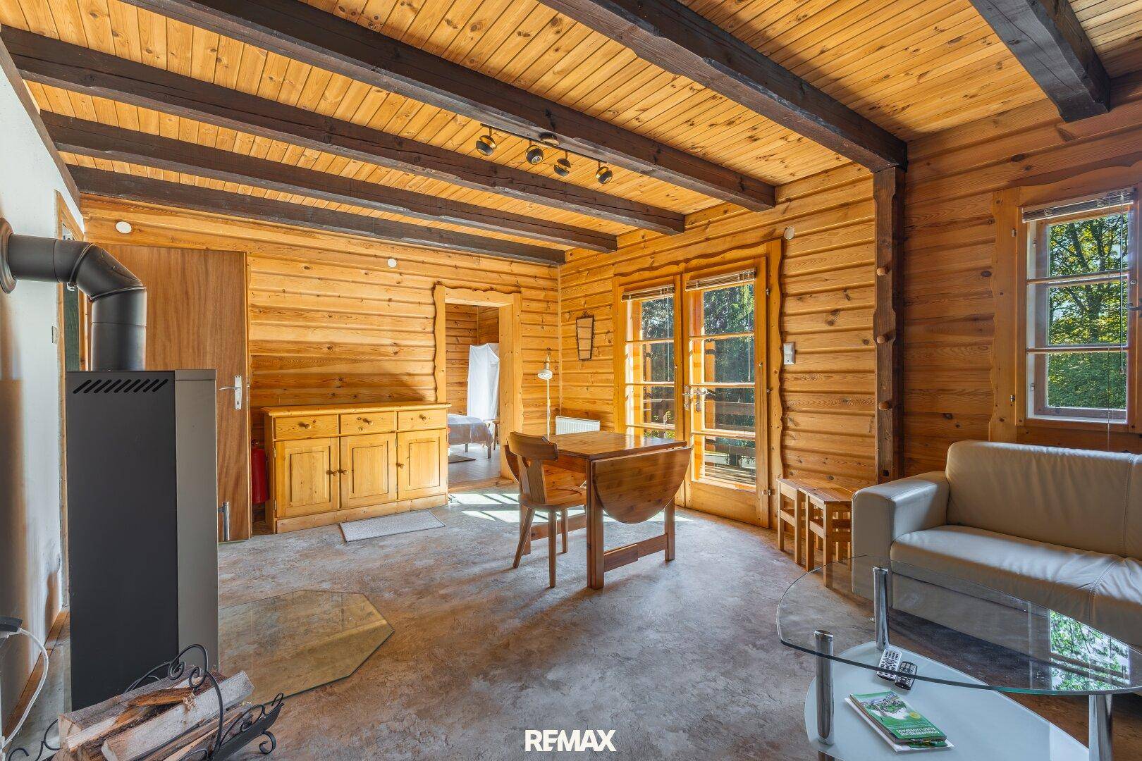 Wohnzimmer mit Kaminofen, Holzwänden und Zugang zur Terrasse.