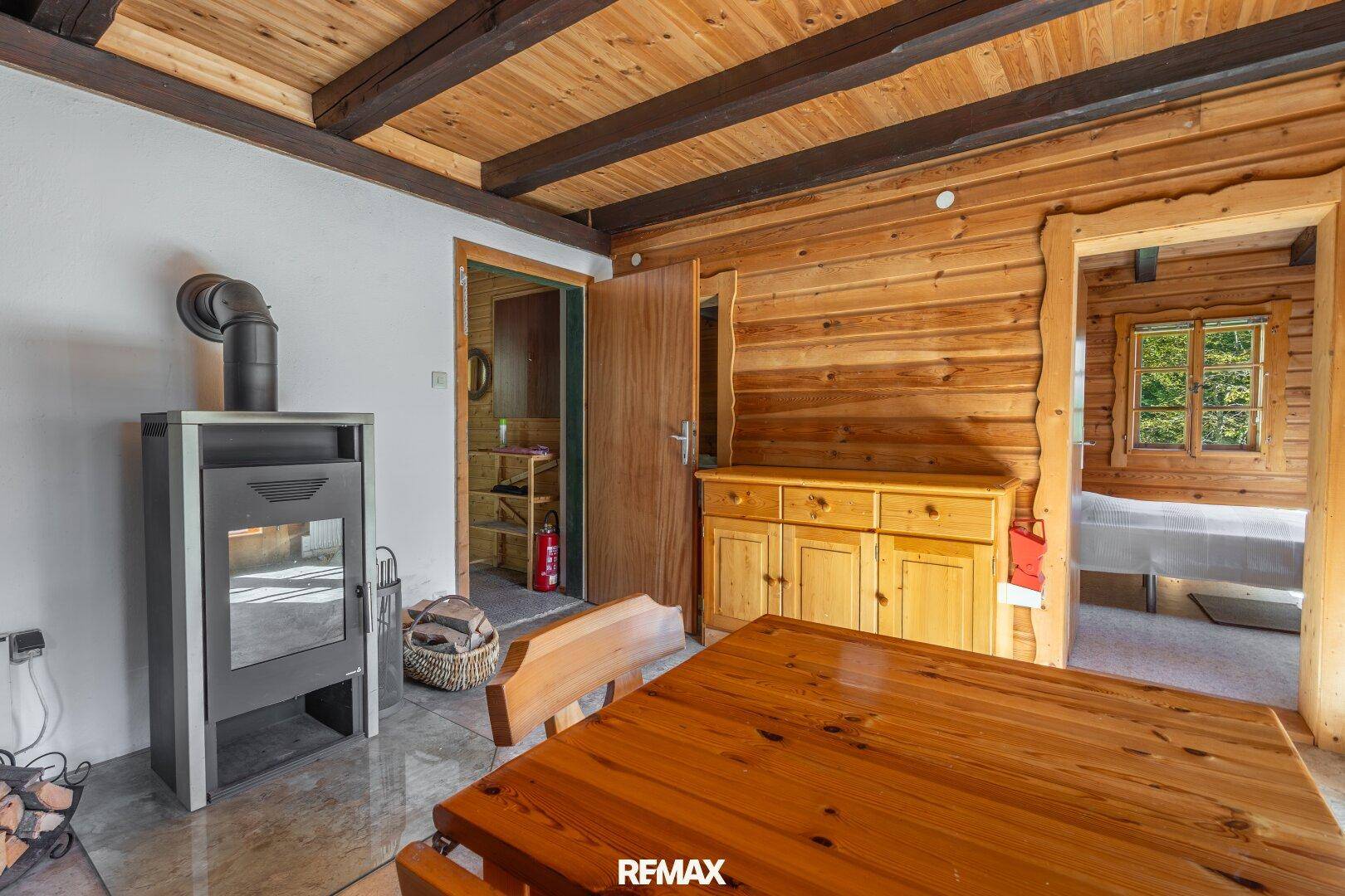 Wohnbereich mit Kaminofen, Holztisch und Blick in ein angrenzendes Schlafzimmer.