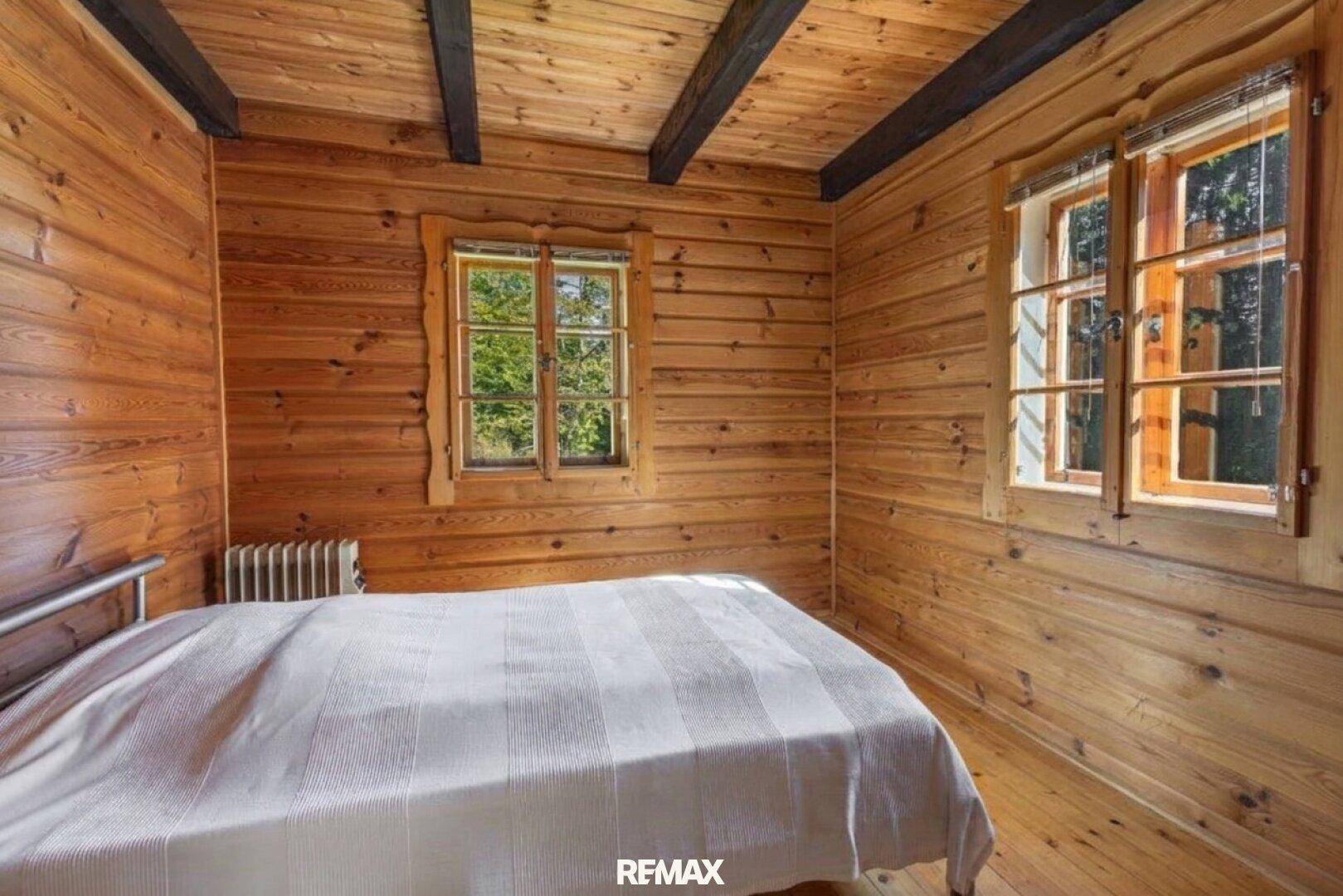 Schlafzimmer mit Holzwänden, Holzboden und Fenstern mit Blick ins Grüne.