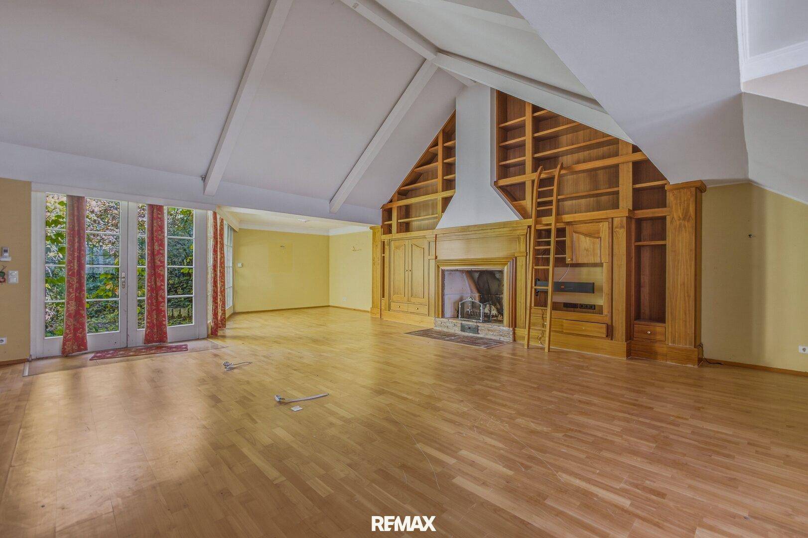 Großzügiges Wohnzimmer mit Holzboden, Kamin und hohen Decken, mit Zugang zum Garten.