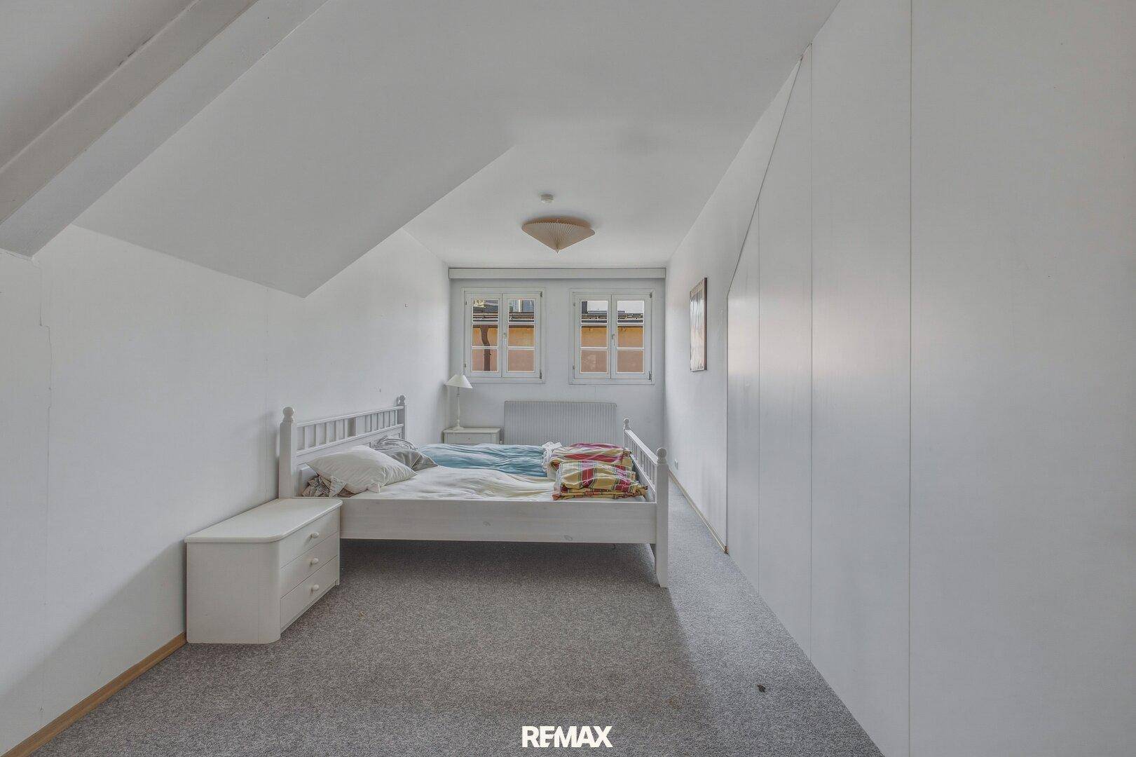 Helles Schlafzimmer im Dachgeschoss mit Teppichboden und schrägen Wänden.