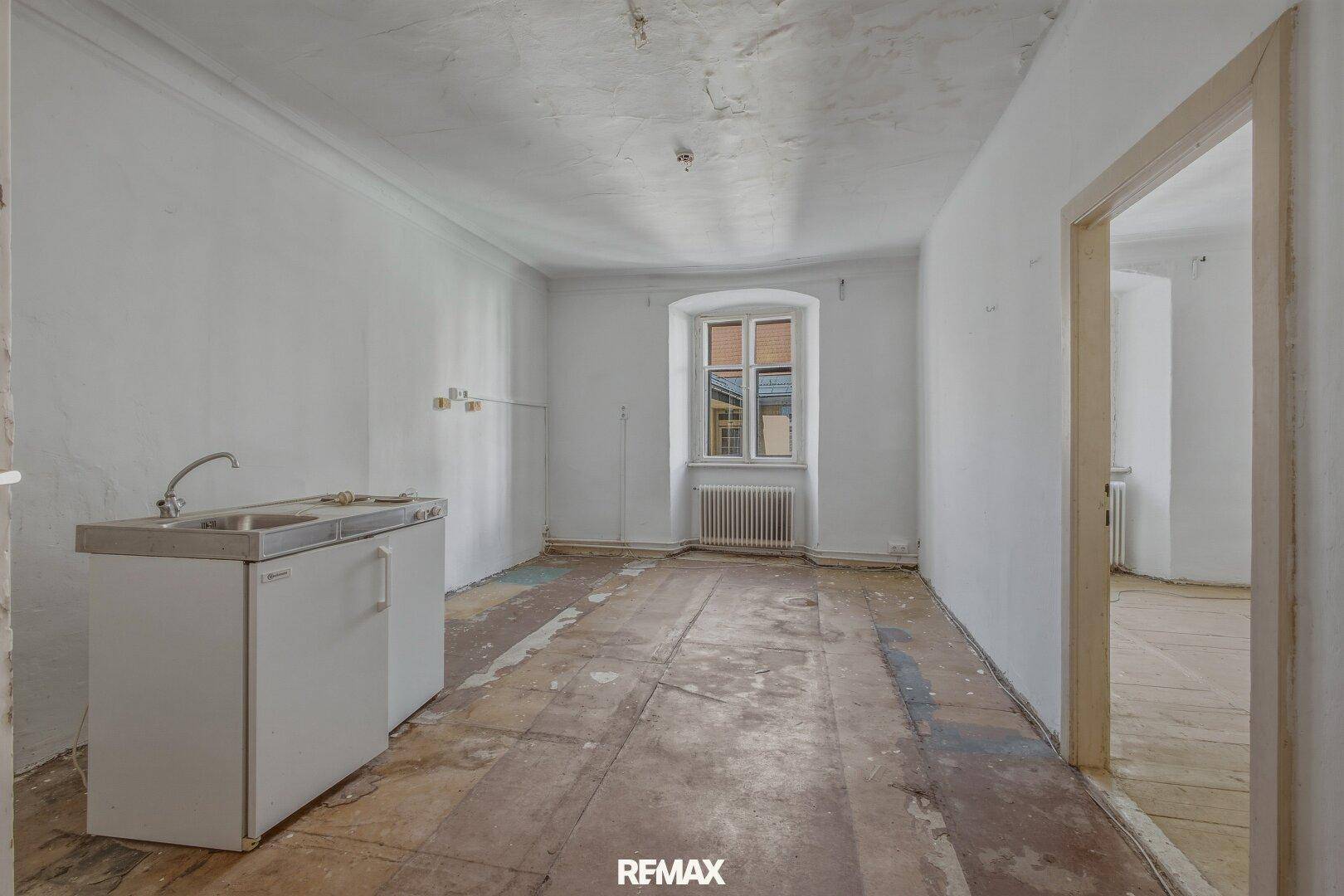 Einfacher Raum mit kleiner Spüle und Fenster, bereit für eine Kücheninstallation.