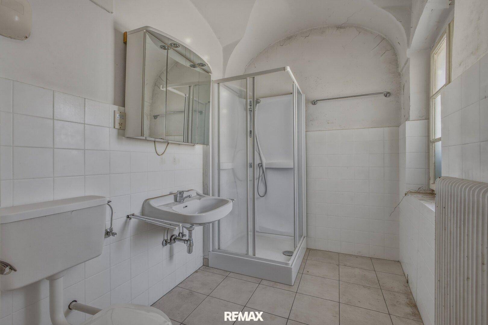 Einfaches Badezimmer mit Dusche, WC und Waschbecken, gefliest und mit Gewölbedecke.