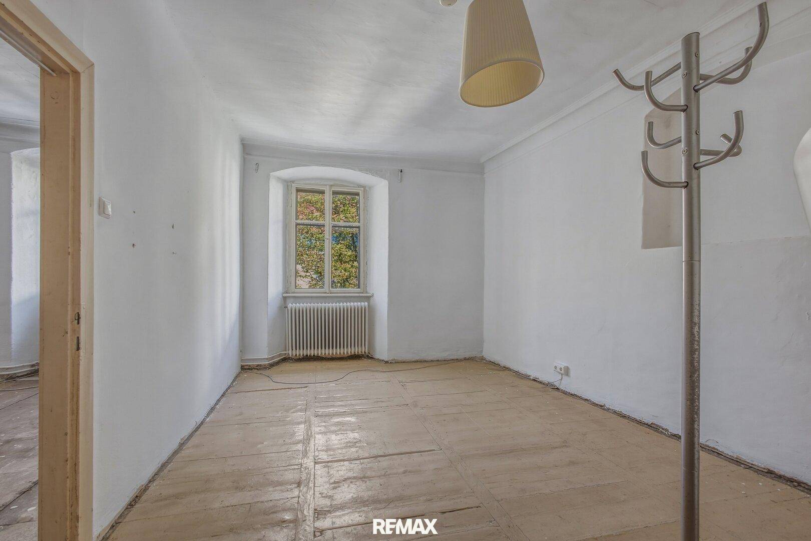 Leerer Raum mit weiß gestrichenen Wänden, einem Fenster und einem alten Heizkörper.