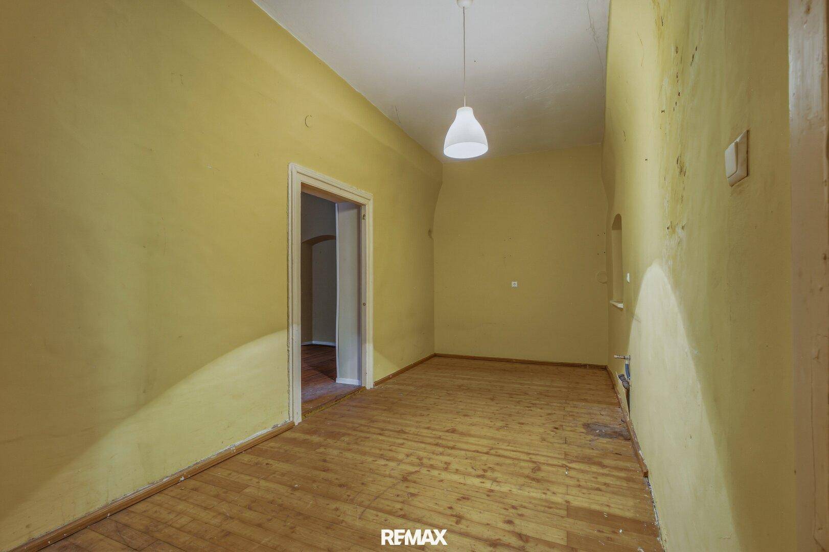 Langer, leerer Raum mit gelben Wänden und Holzdielenboden, ideal für eine Renovierung.
