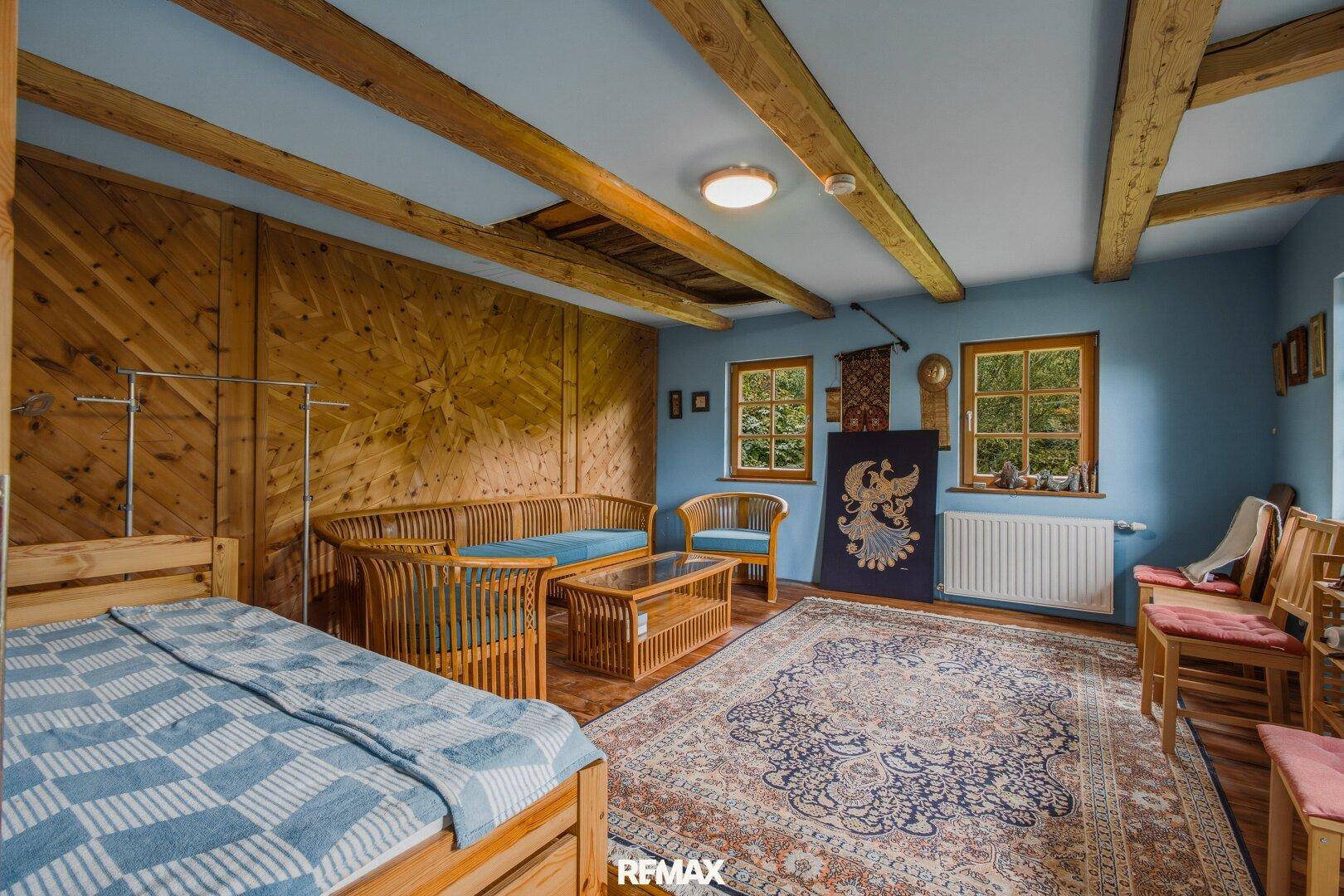 Gemütliches Wohnzimmer mit Holzwänden, Holzbalkendecke und traditionellem Teppich.
