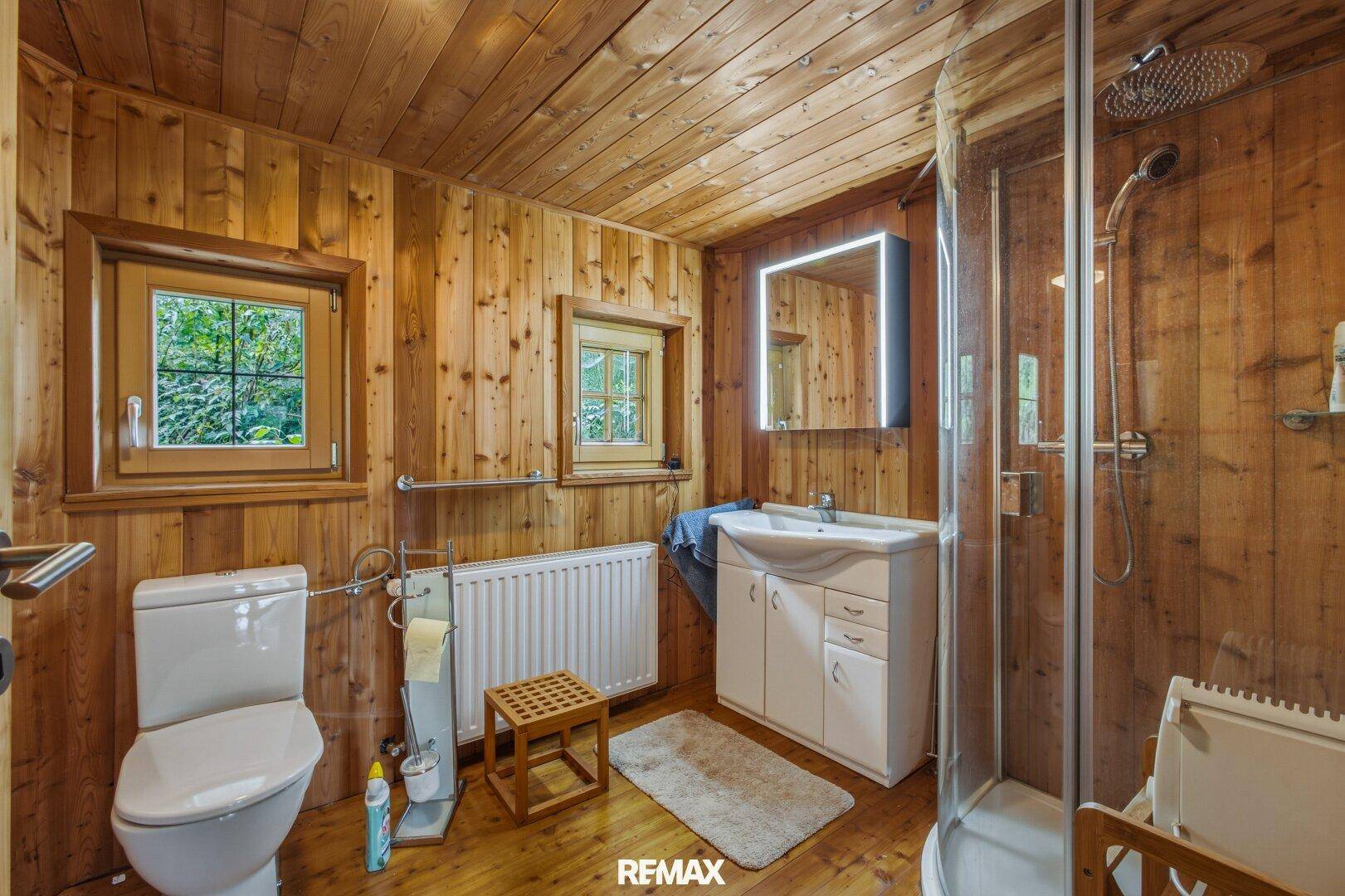 Badezimmer mit Holzwänden, Holzboden, Dusche und Fenster.