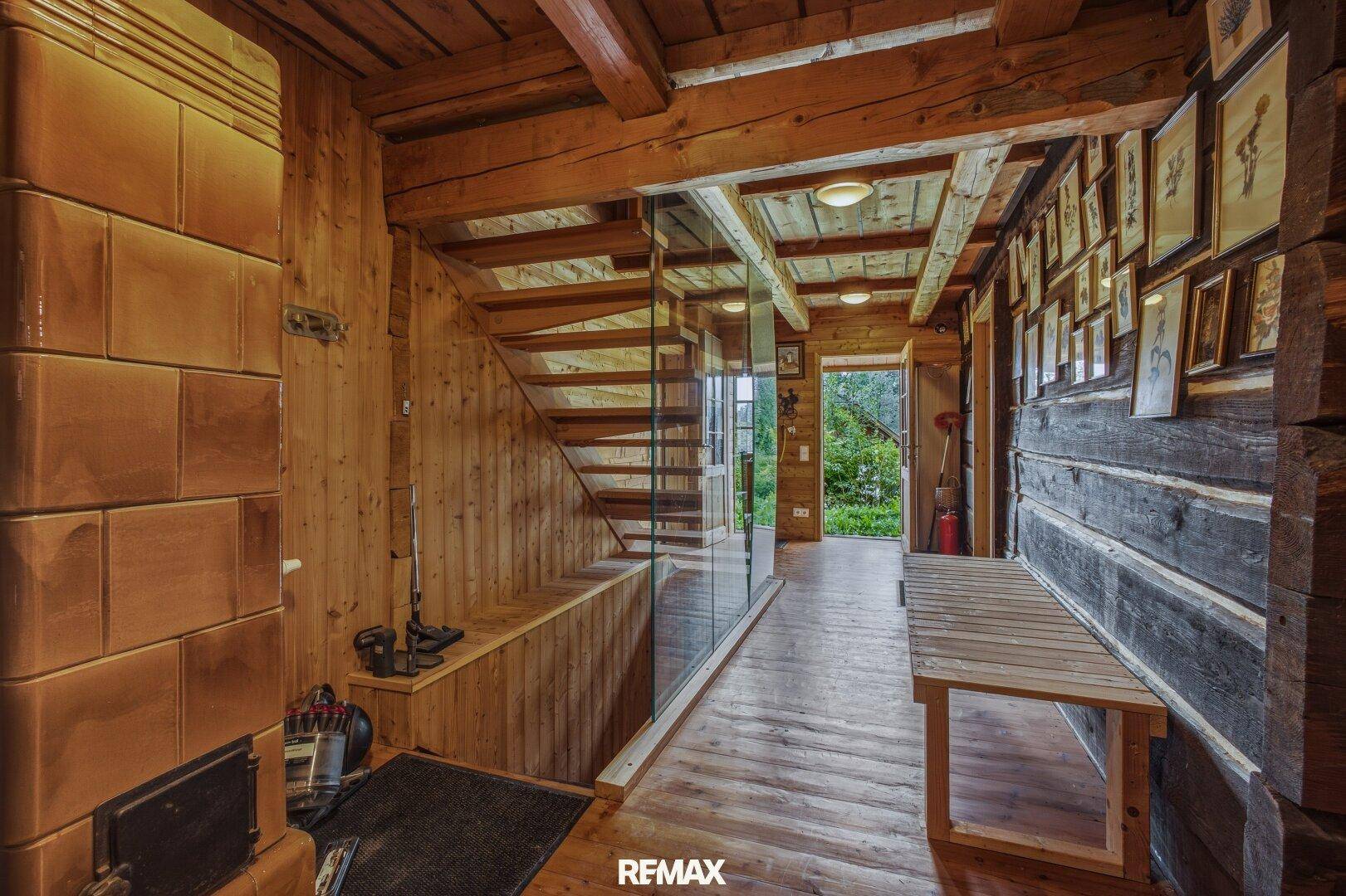 Flur mit Holzboden, Holzwänden, Kachelofen und offener Holztreppe.