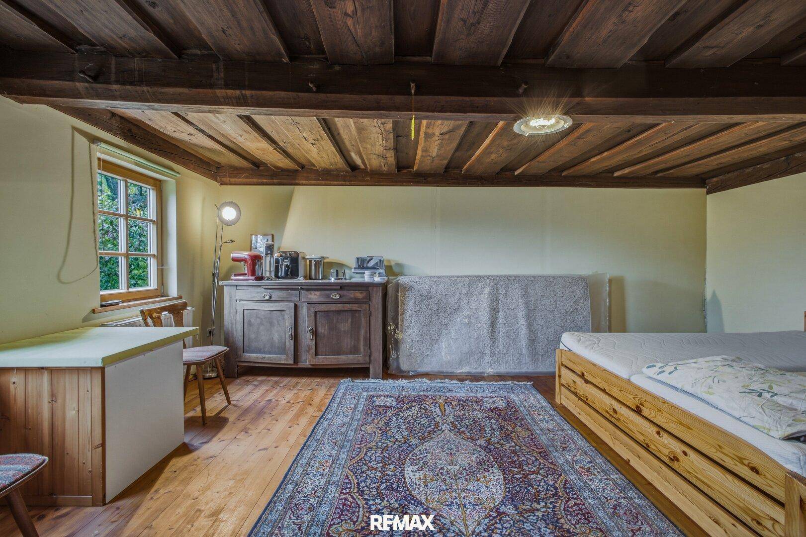 Schlafzimmer mit Holzbalkendecke, Holzboden und traditionellem Teppich.
