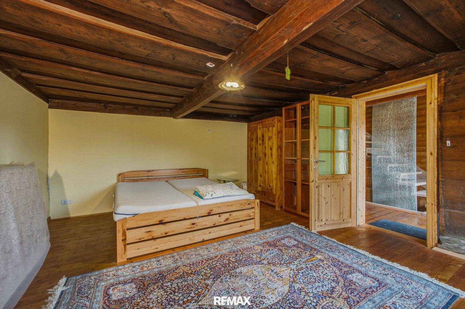 Schlafzimmer mit Holzbalkendecke, Holzboden und traditionellem Teppich.