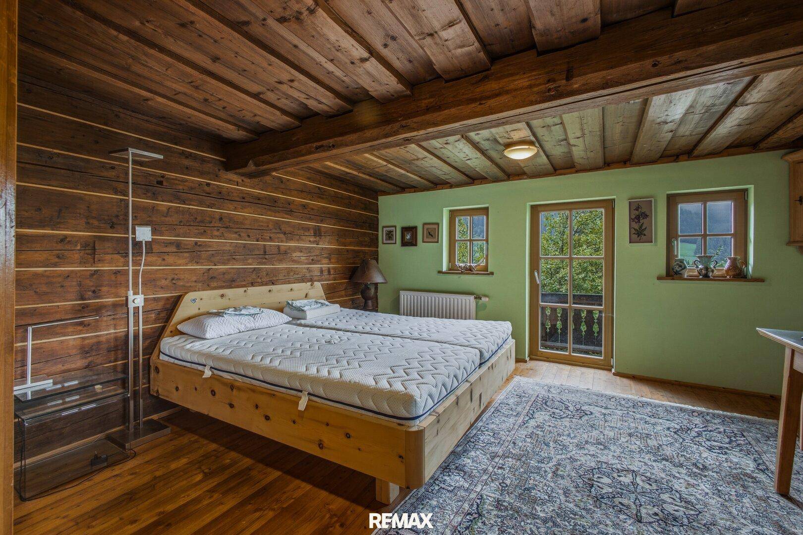Schlafzimmer mit Holzboden, Holzwänden, Balkonzugang und grüner Aussicht.