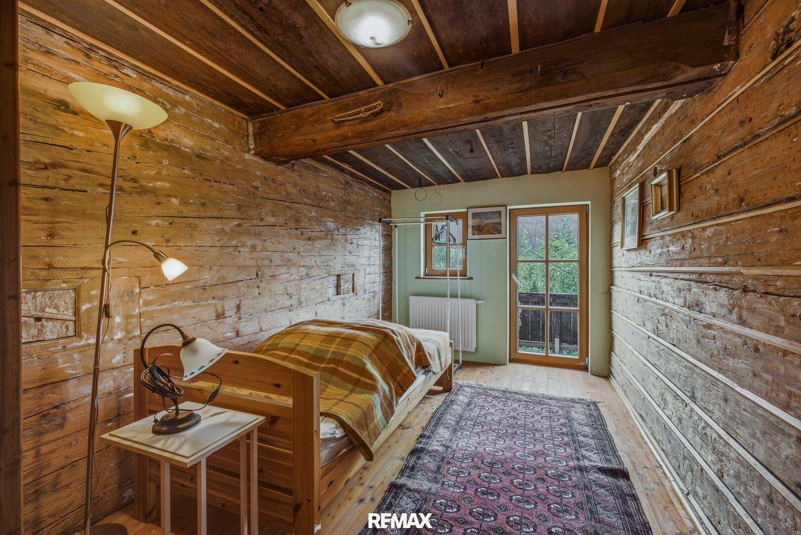 Gemütliches Schlafzimmer mit Holzwänden, Holzboden und Balkonzugang.