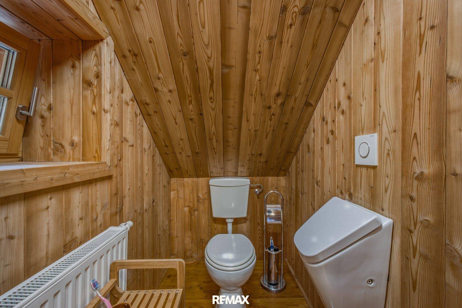 Kleines WC mit Holzwänden, Holzboden, Toilette und Urinal.