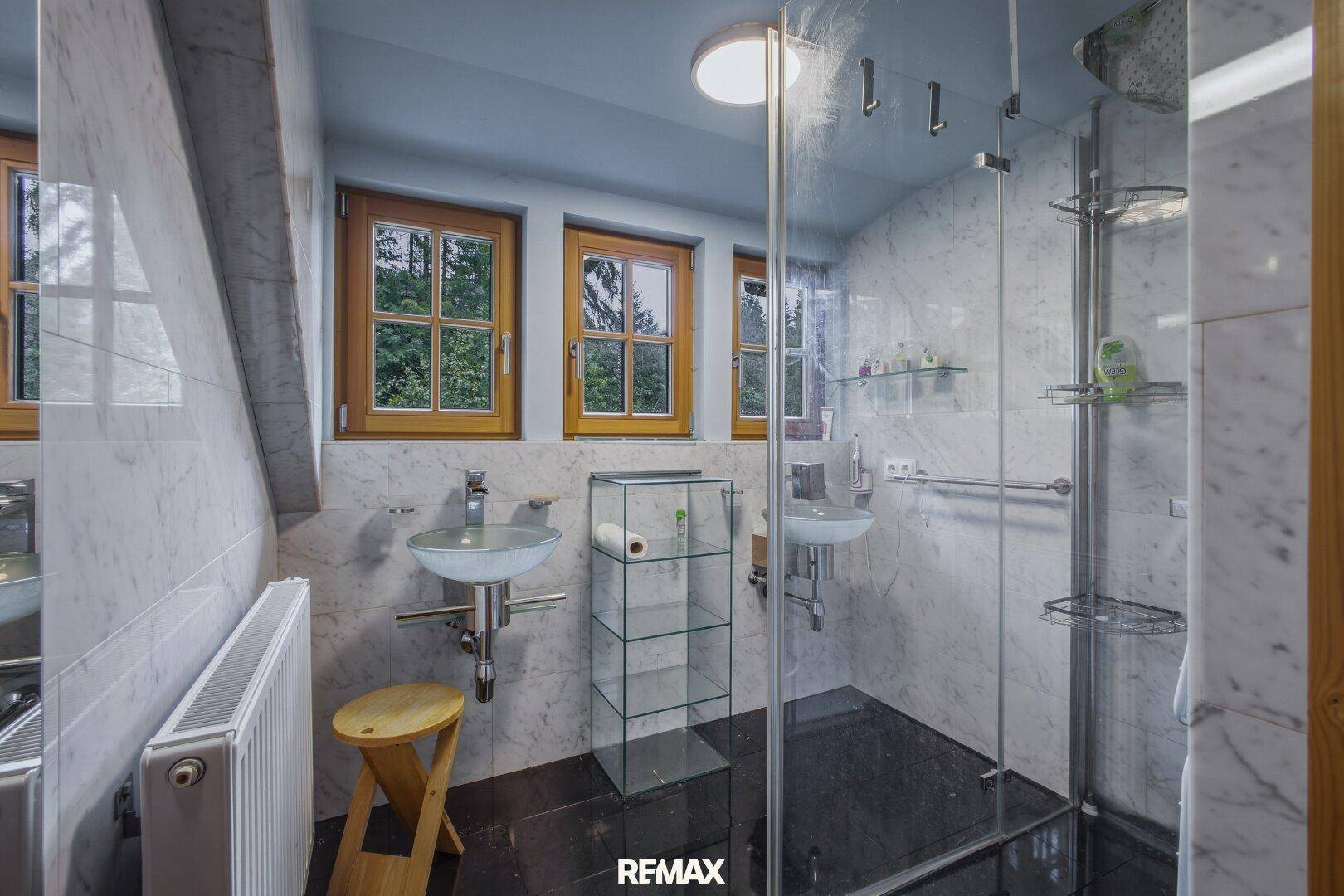Modernes Badezimmer mit Marmorfliesen, Dusche, zwei Waschbecken und Fenstern.