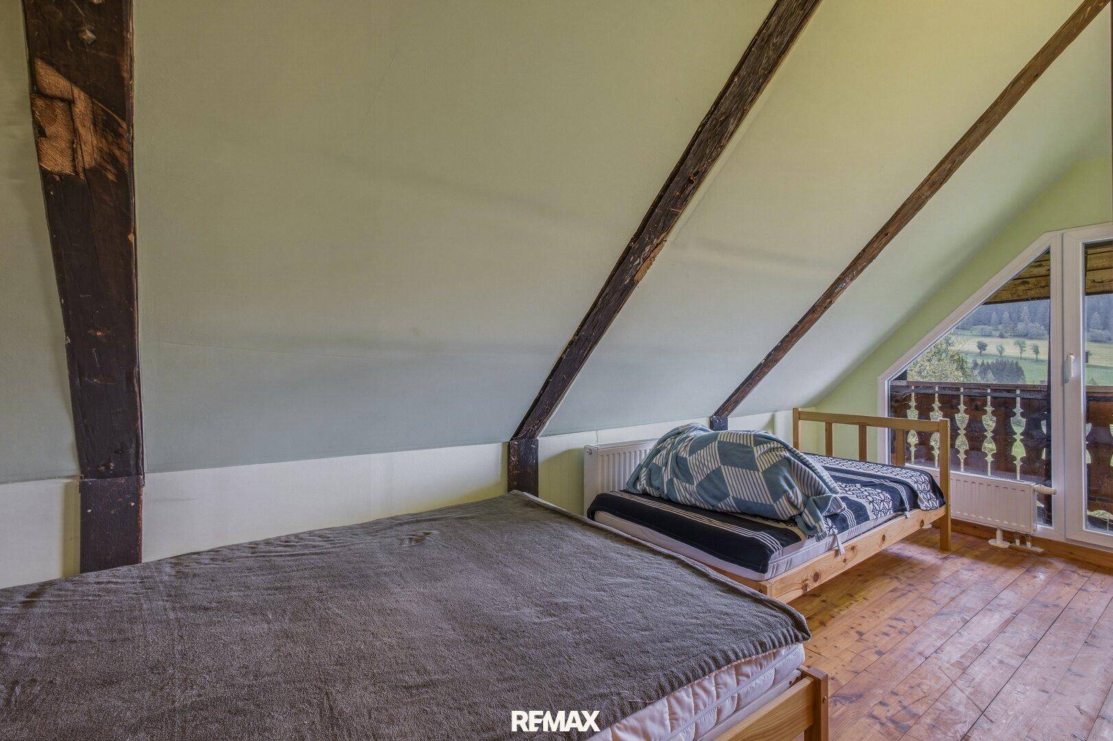 Helles Schlafzimmer im Dachgeschoss mit Holzboden, Dachschrägen und Balkonzugang.