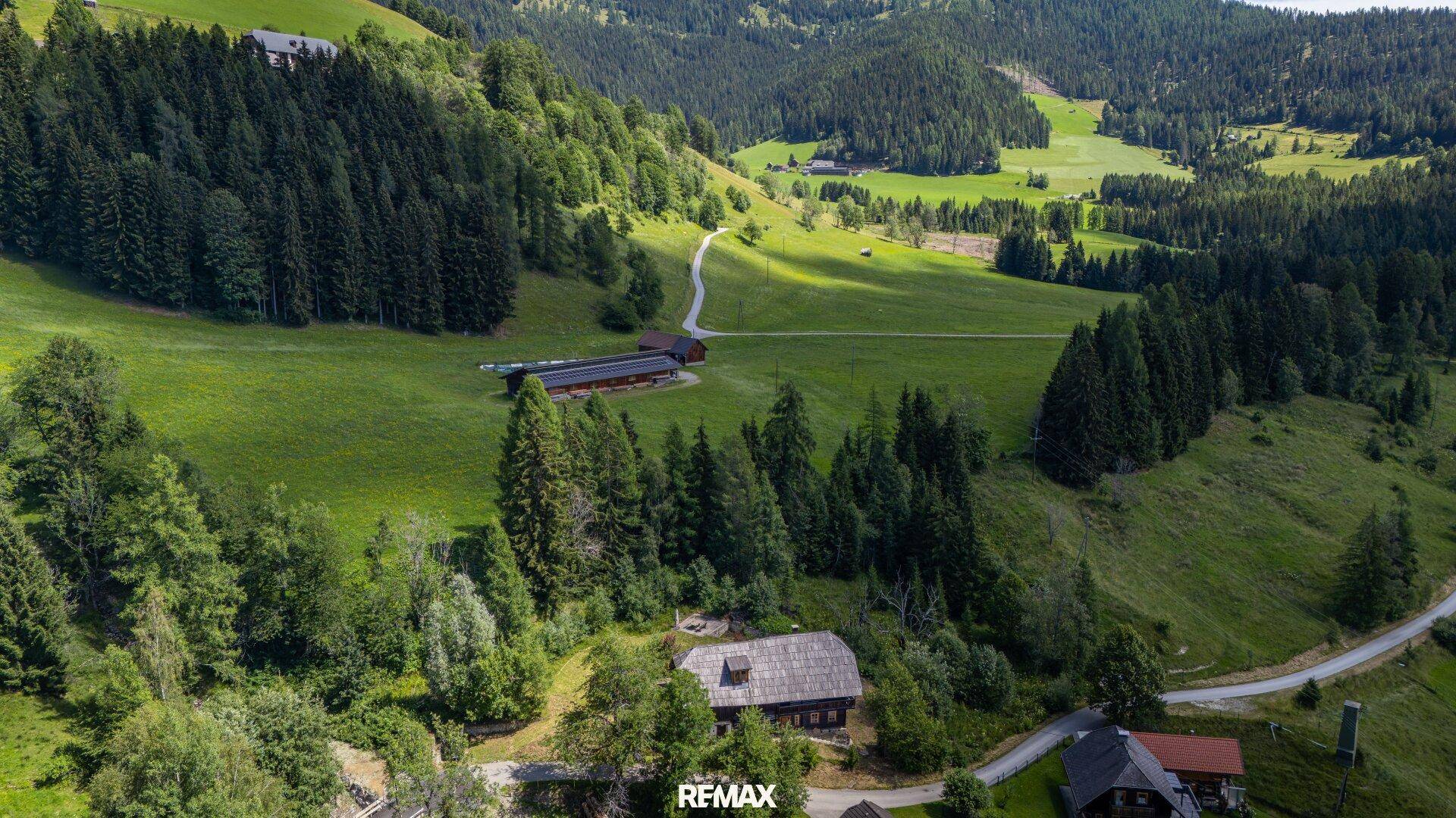 Weitläufige Luftaufnahme der Liegenschaft, eingebettet in eine malerische grüne Hügellandschaft mit Wäldern.